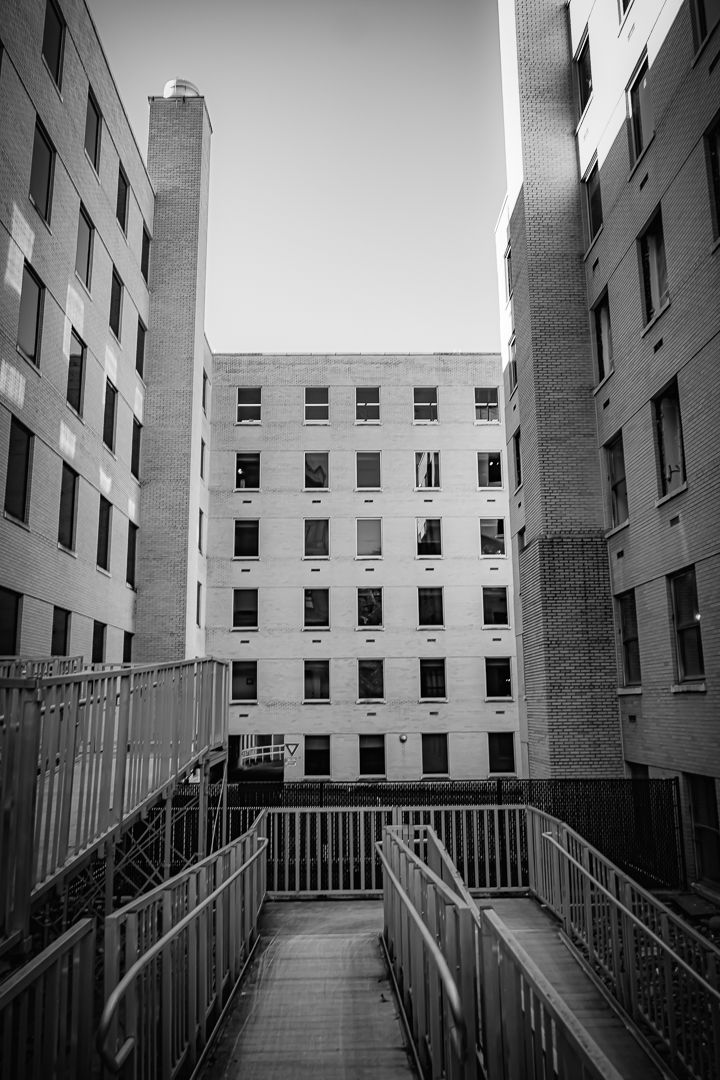 Symmetrical black and white urban courtyard view between brick apartment buildings with metal railing walkway.