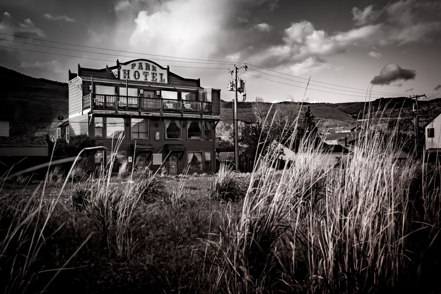 Abandoned vintage hotel building surrounded by tall dry grass under moody sky in black and white photography.
