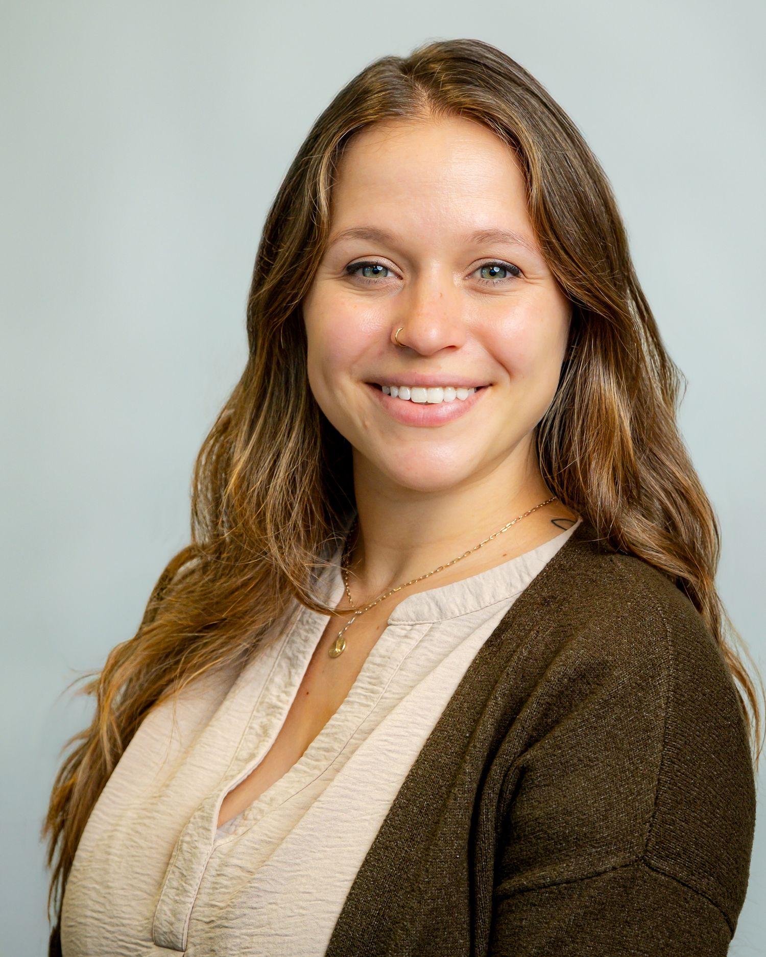 Professional headshot of a smiling young woman with long brown hair wearing a dark cardigan and delicate necklace.headshot