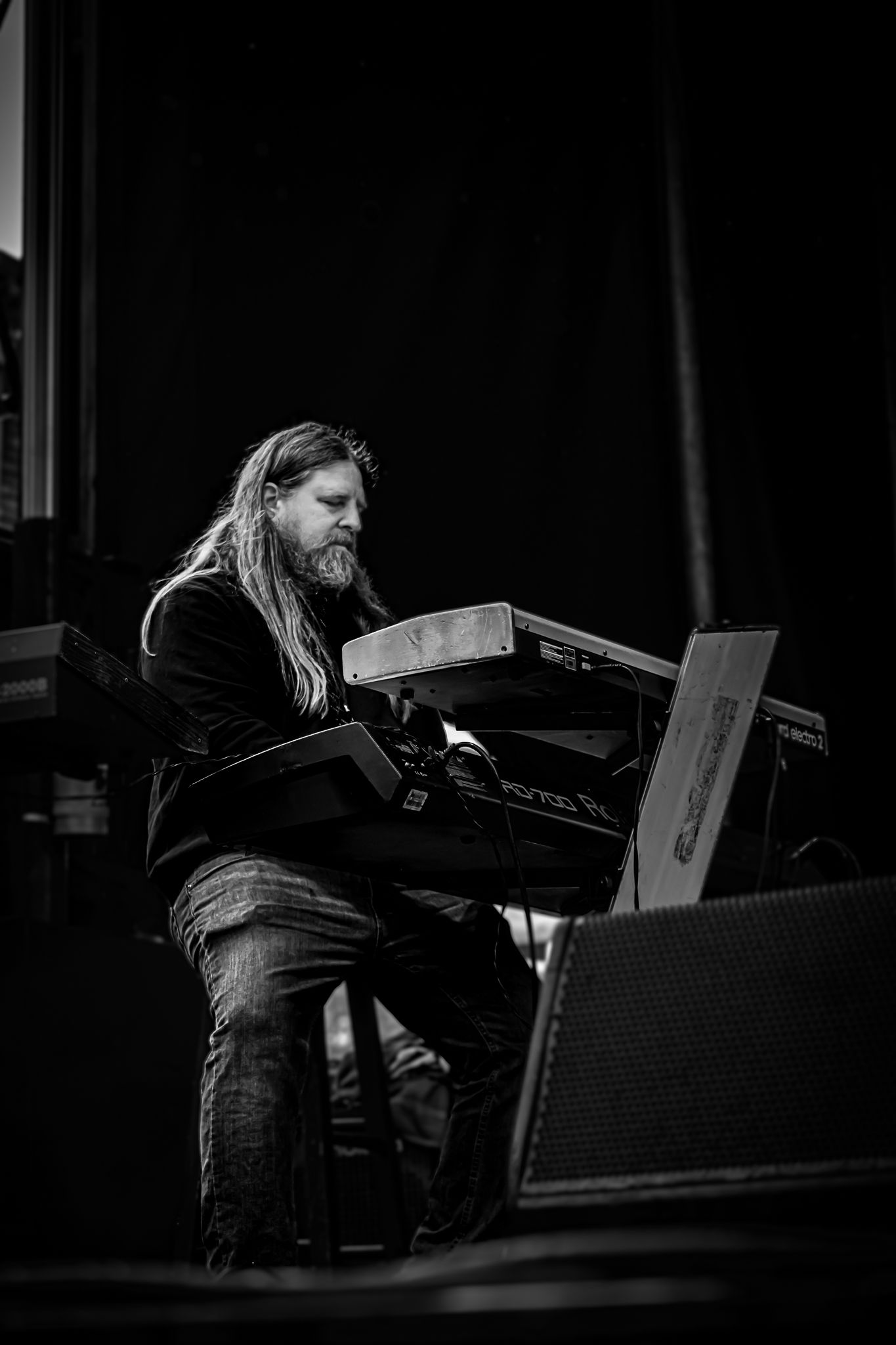 Black and white photo of a long-haired male musician playing keyboard synthesizer on stage.