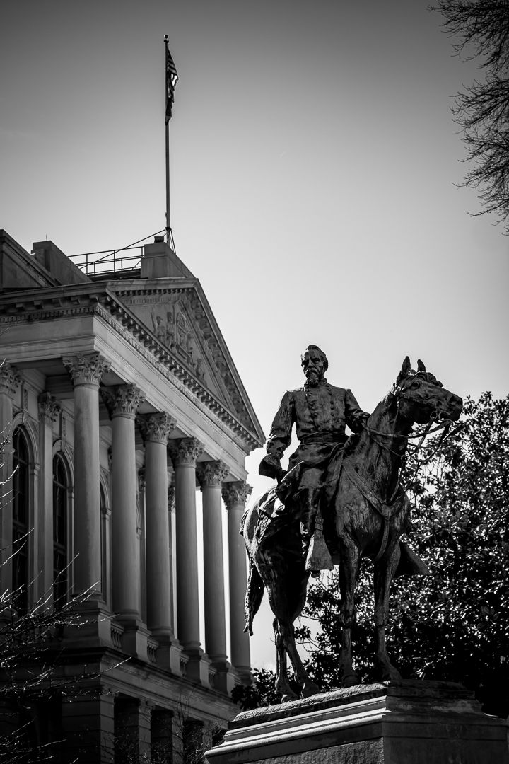 Black and white photo of an equestrian statue in front of a neoclassical building with columns and an American flag.