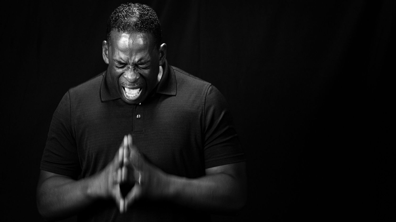 Black and white portrait of a man in prayer pose, eyes closed, hands clasped together in devotion.