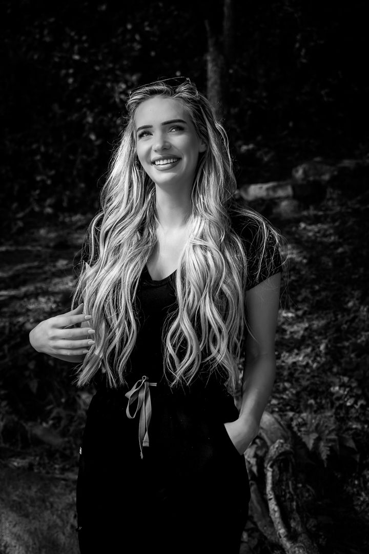 Smiling young blonde woman with long wavy hair poses outdoors in a black and white photo.