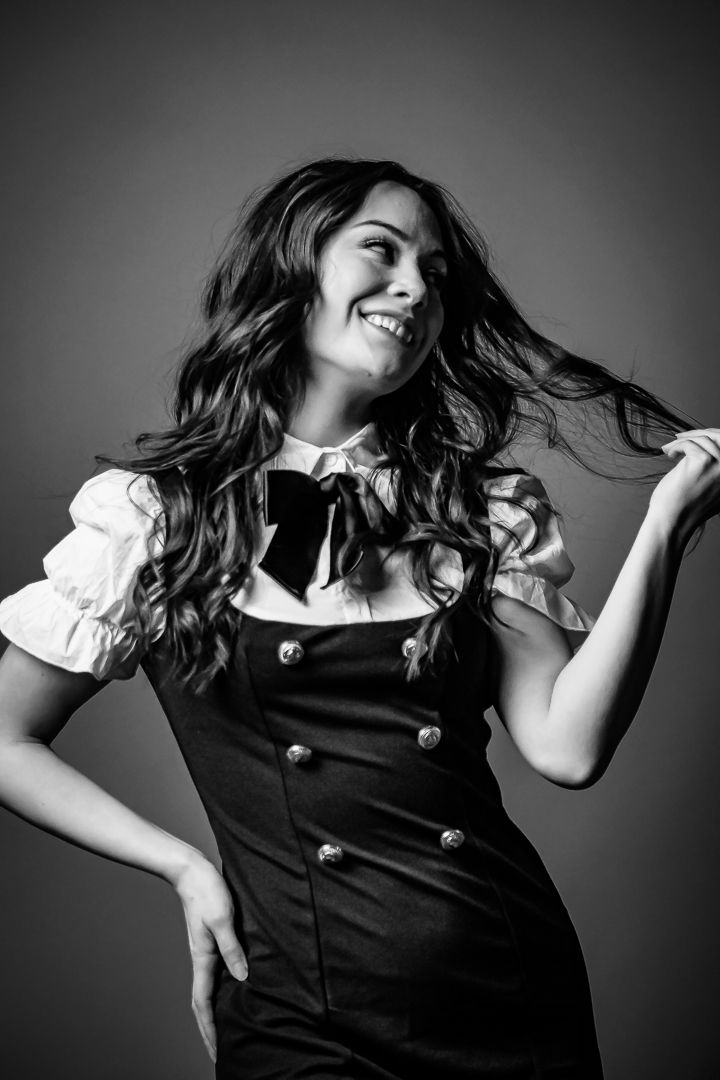 Black and white portrait of a smiling woman in a vintage dress with bow tie, playfully tossing her long wavy hair.