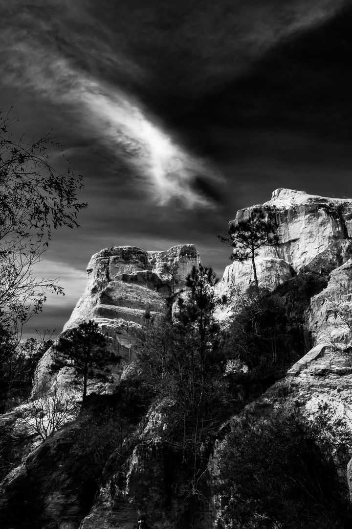 Striking black and white image of rugged rock formations with pine trees under a swirling dramatic cloudy sky.
