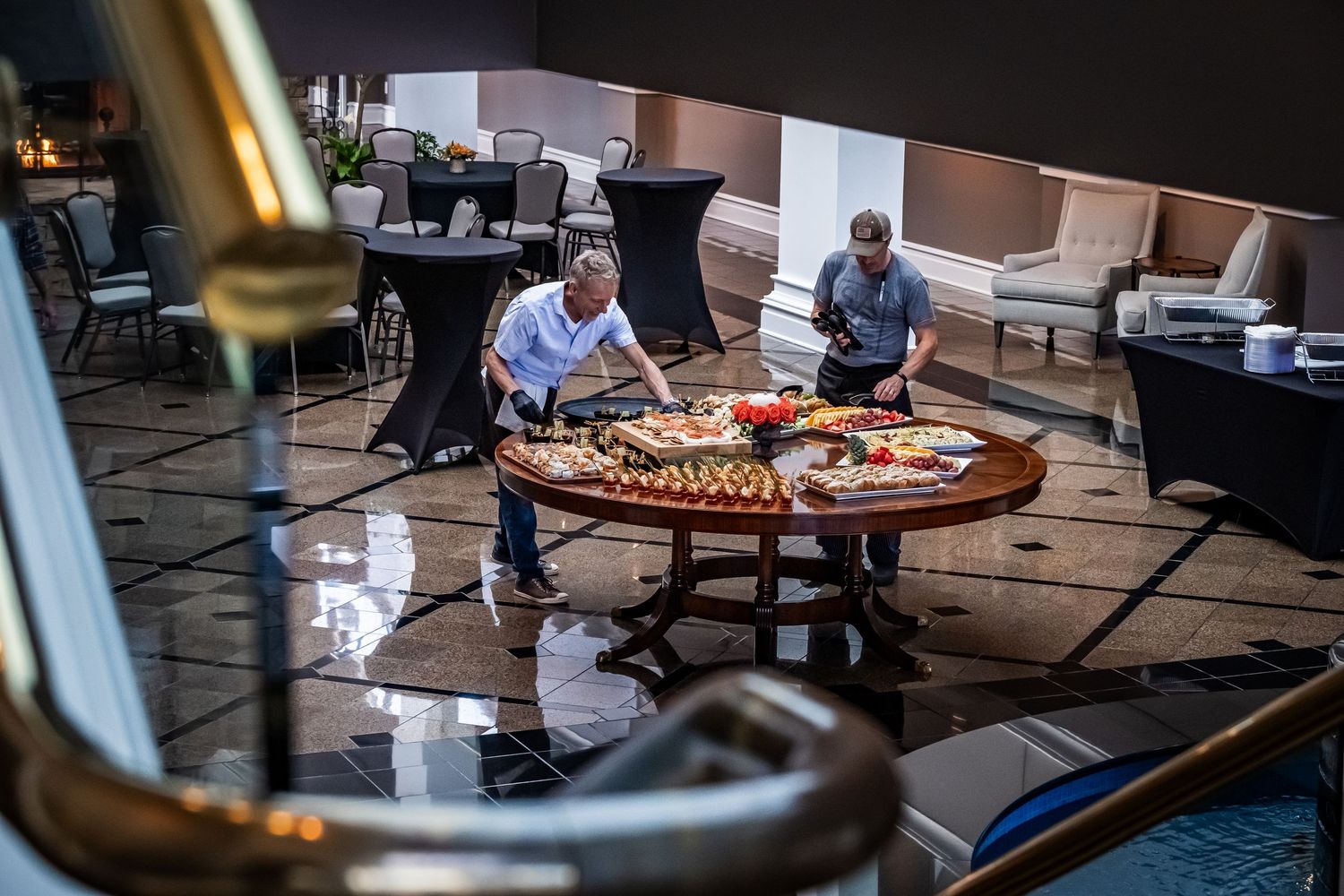 Two catering staff arranging a large round food display table in an upscale hotel venue.