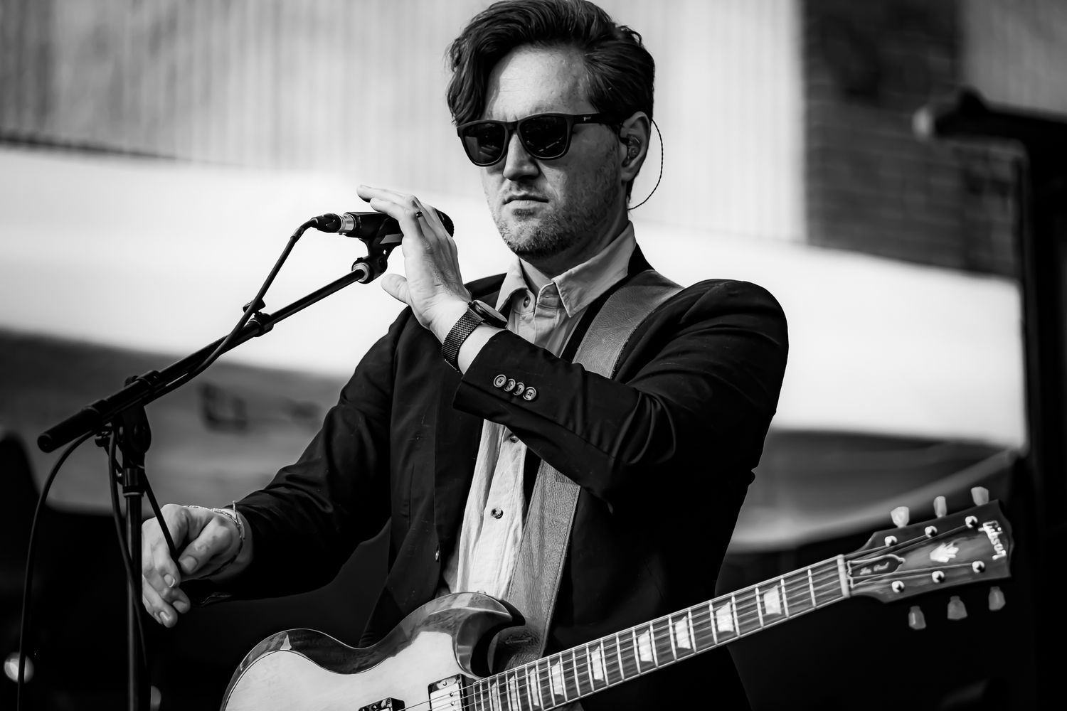Male guitarist wearing sunglasses performing live on stage with electric guitar at outdoor concert.