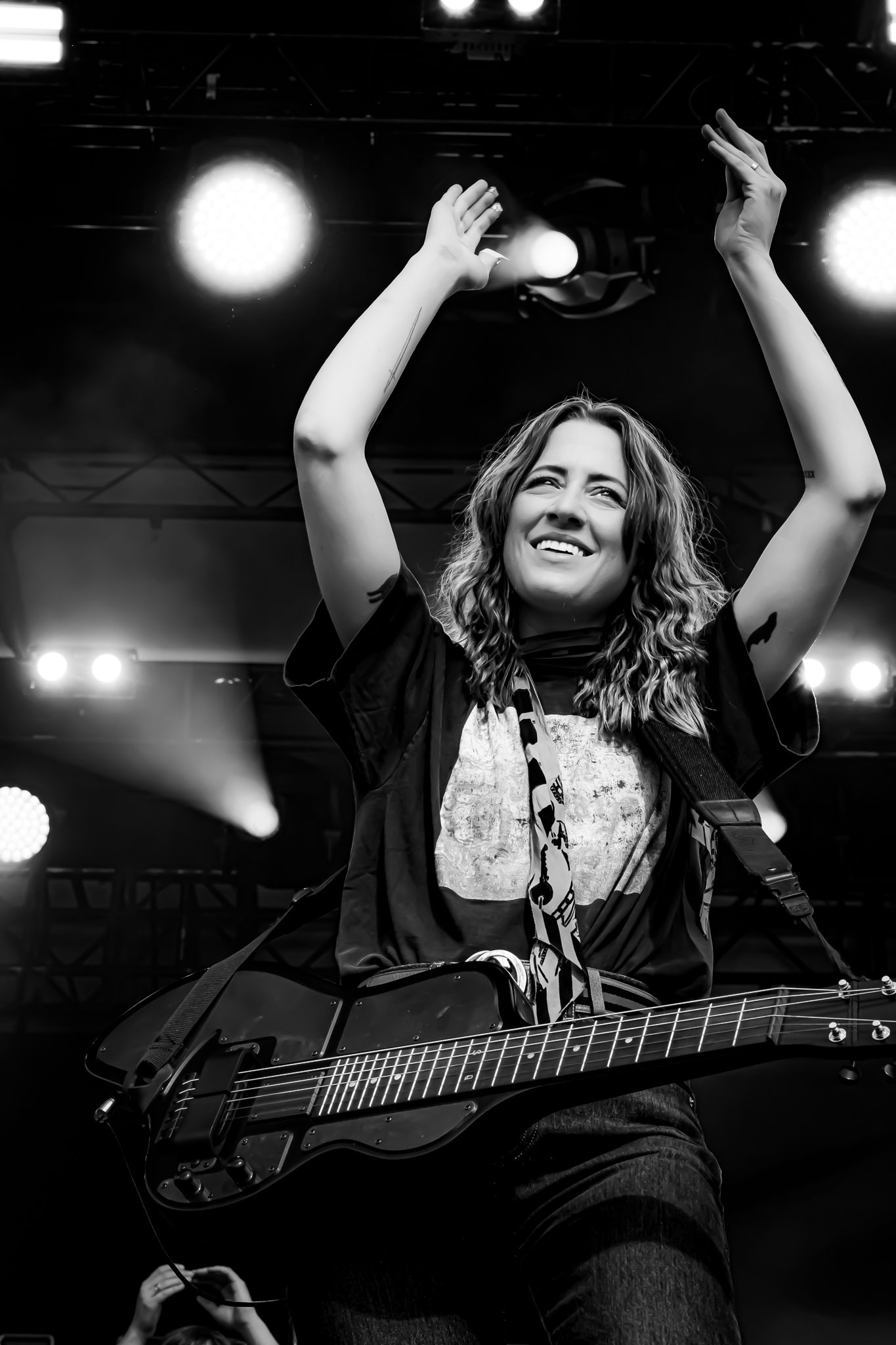 Smiling female guitarist raising hands on stage in black and white concert photography.