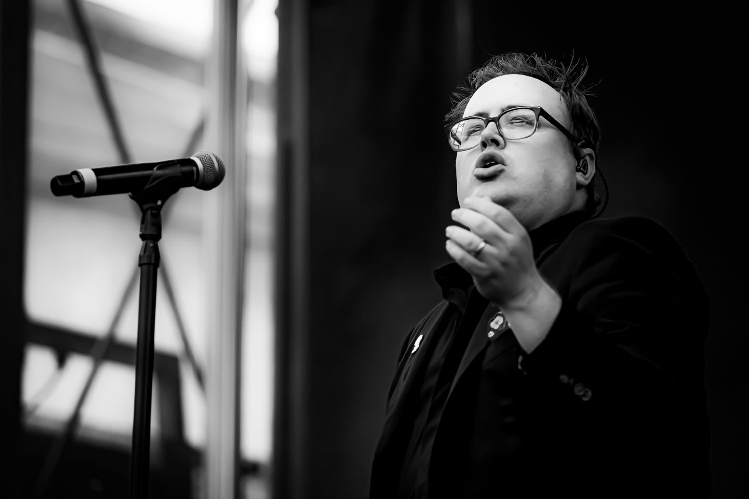 Black and white portrait of male singer performing at microphone stand at outdoor venue.