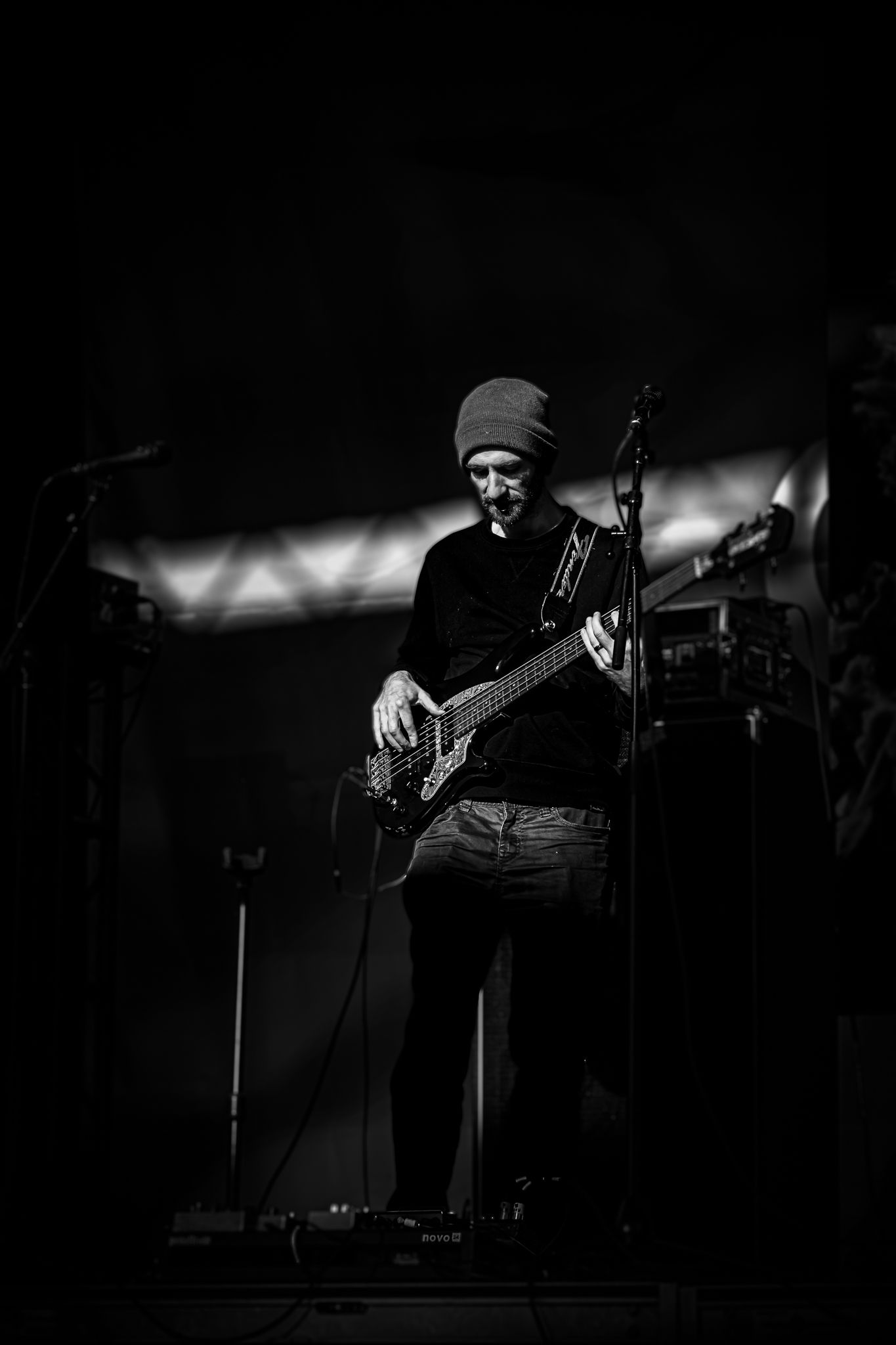 Black and white photo of a guitarist performing on a dark stage wearing a beanie hat.