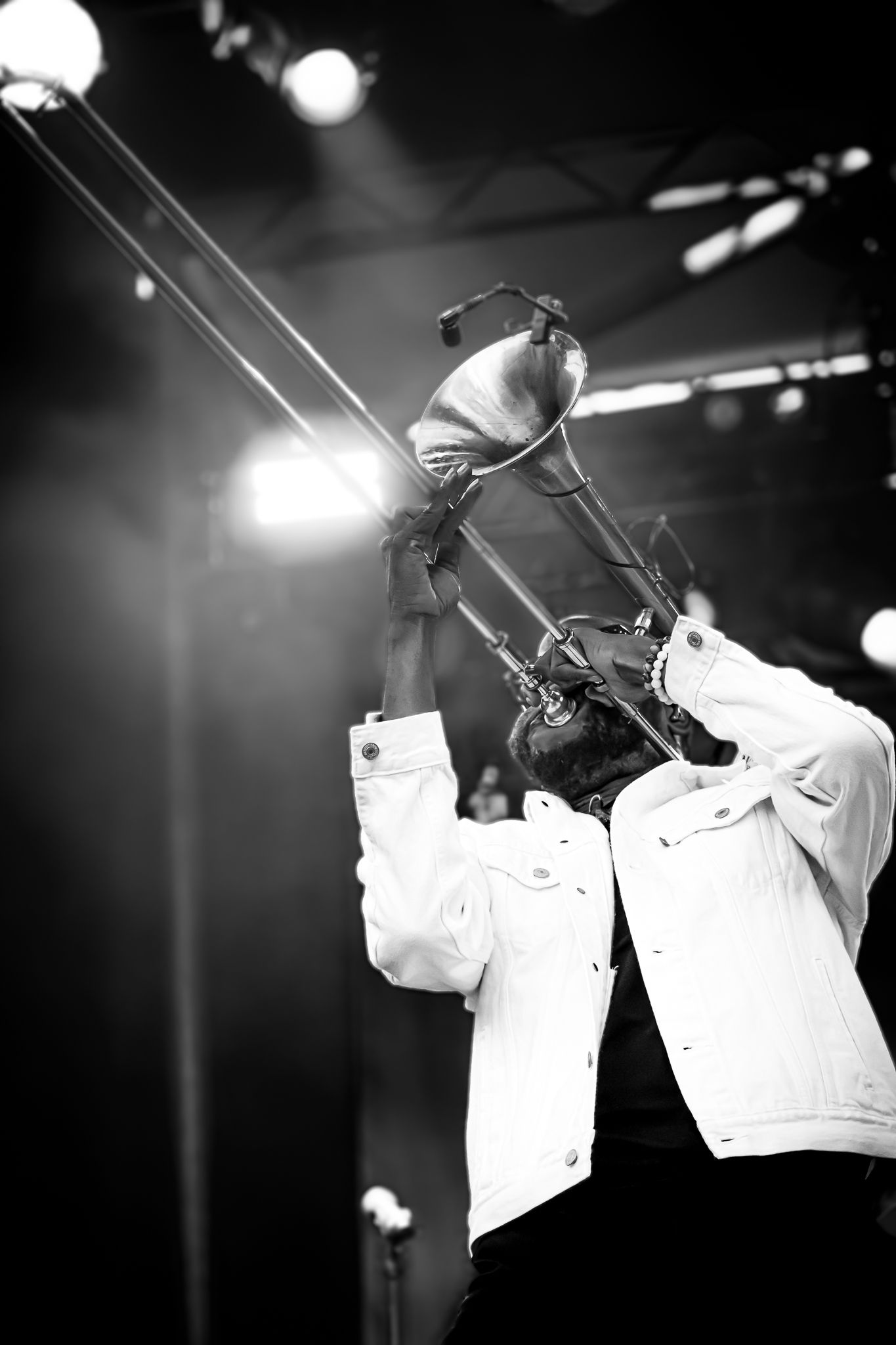Black and white photo of trombone player lifting instrument overhead under stage lights.