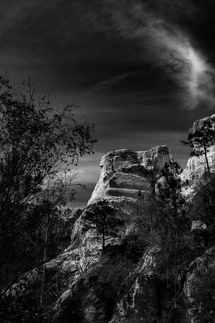 Black and white rocky outcrop with stepped stone formations framed by dark trees.