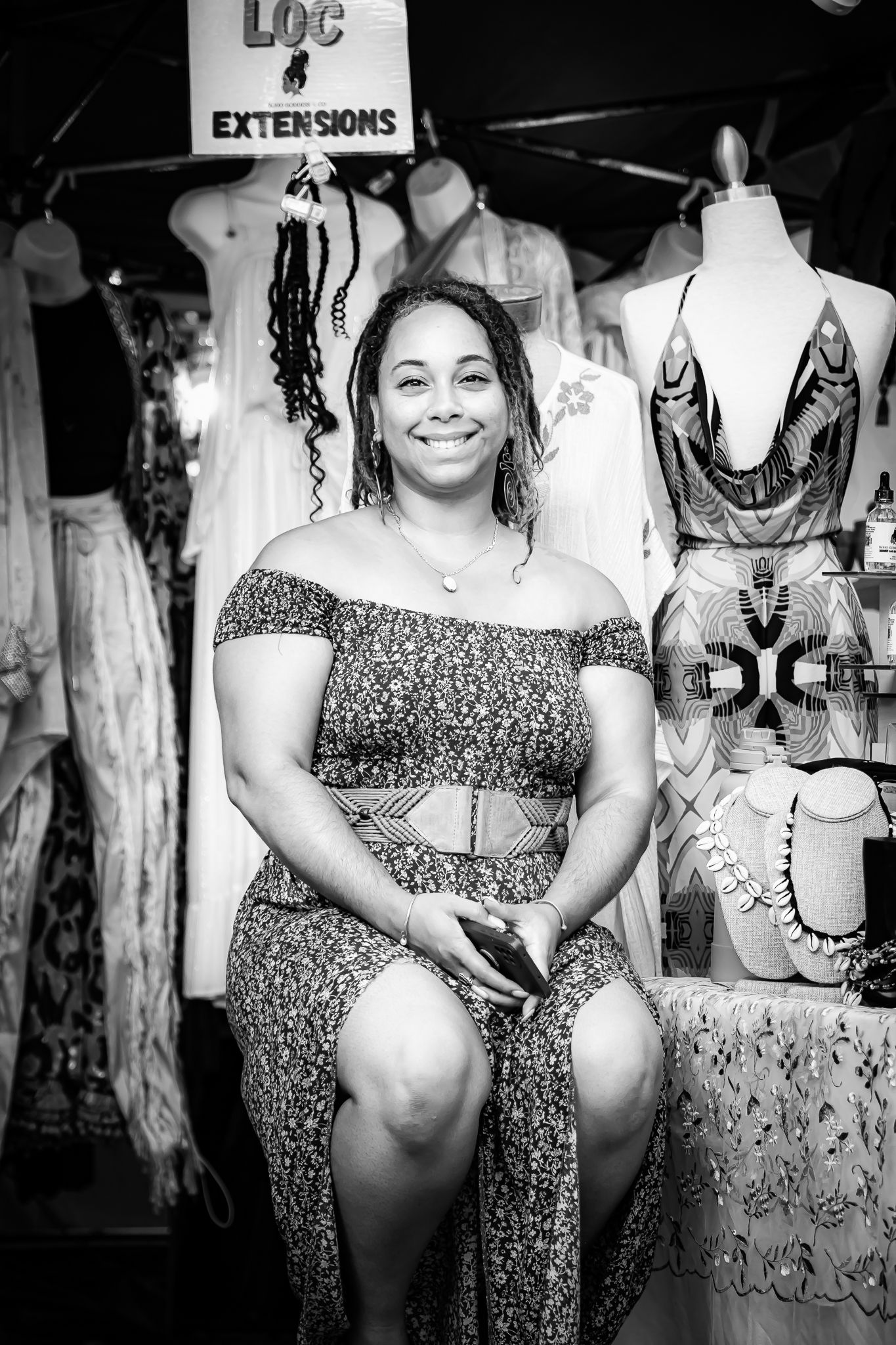 Woman smiles while seated at a loc extensions vendor booth in a black and white photo.