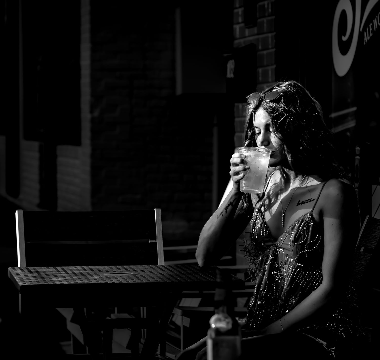 Black and white photo of a woman sipping coffee at an outdoor cafe table at night.