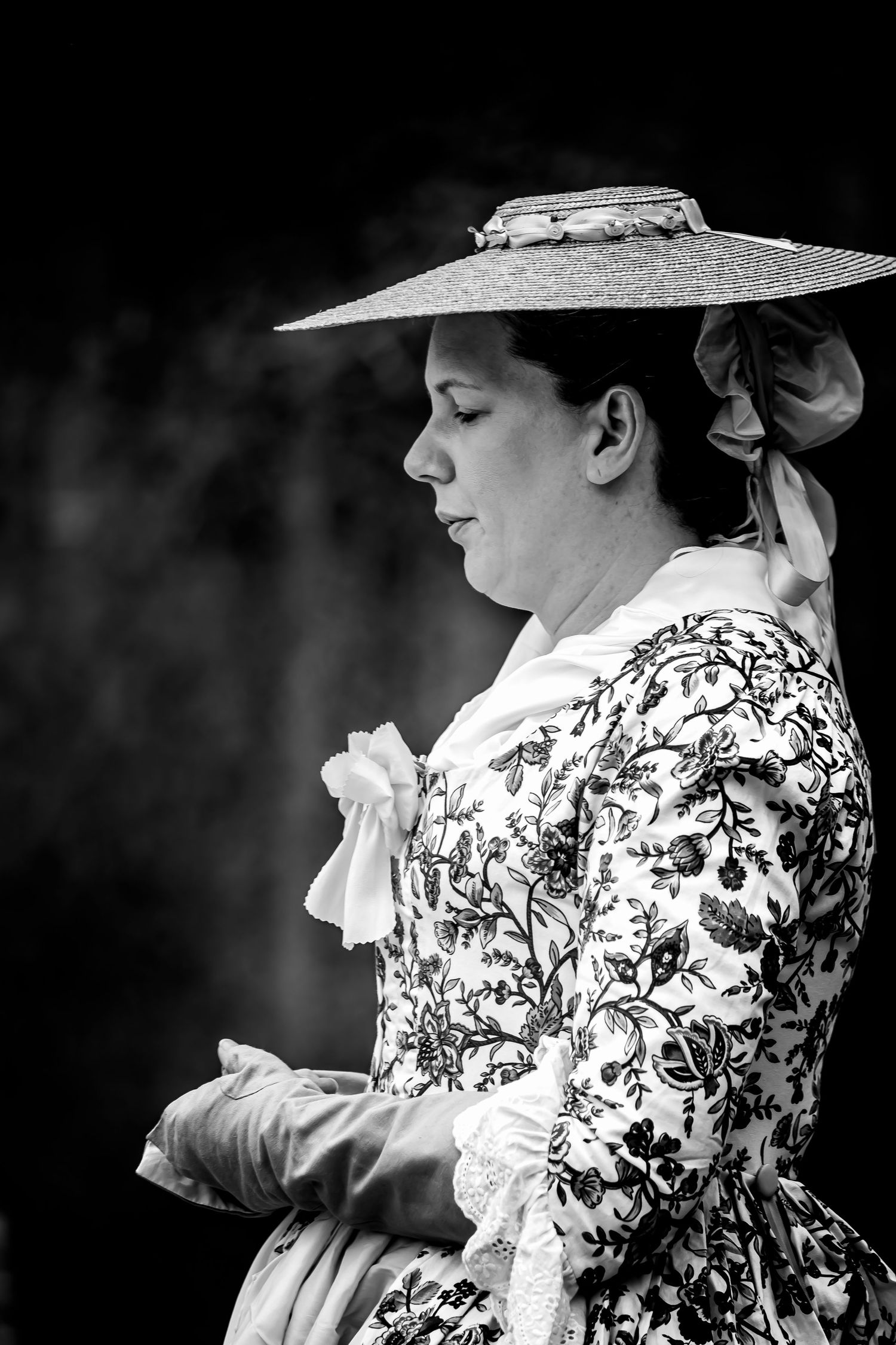 Woman in elegant 18th century floral dress and wide-brim hat, side profile black and white portrait.