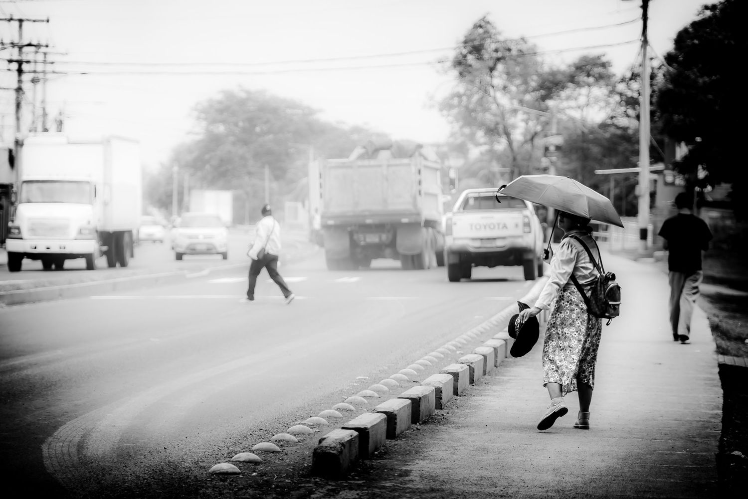 Woman with umbrella walks along busy roadside in atmospheric black and white street photography. Street photography North Georgia Nicaragua