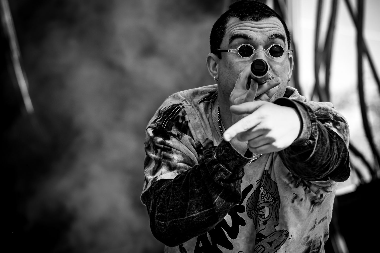 Black and white photo of a theatrical performer wearing a clown nose and round glasses on a smoky stage.
