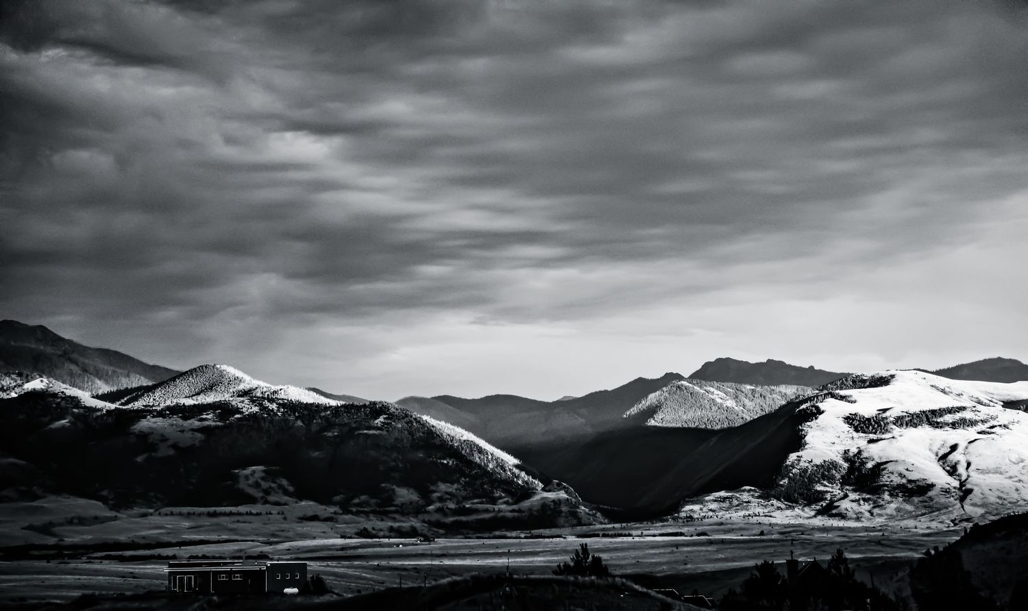 Black and white mountain landscape with snow-capped peaks under dramatic storm clouds.
