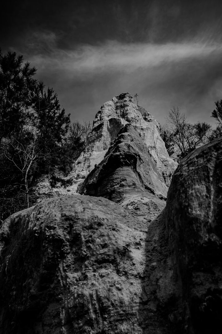 Black and white low-angle view of rugged rock spire with cave opening below.