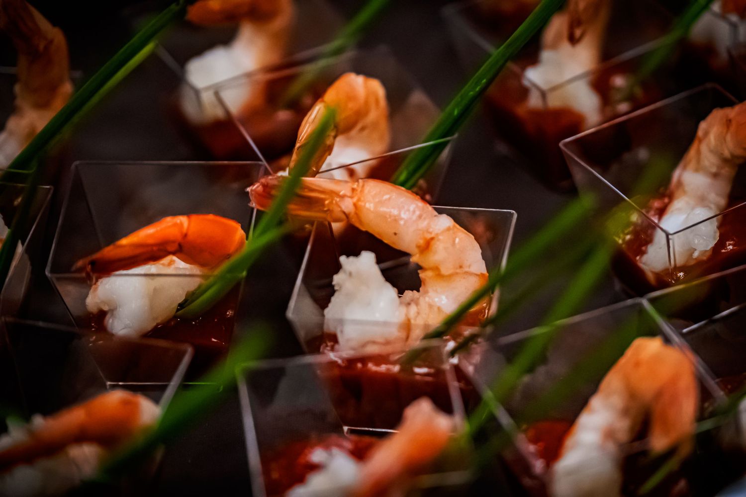 Shrimp cocktail appetizers served in small square plastic cups with cocktail sauce and garnished with chives.