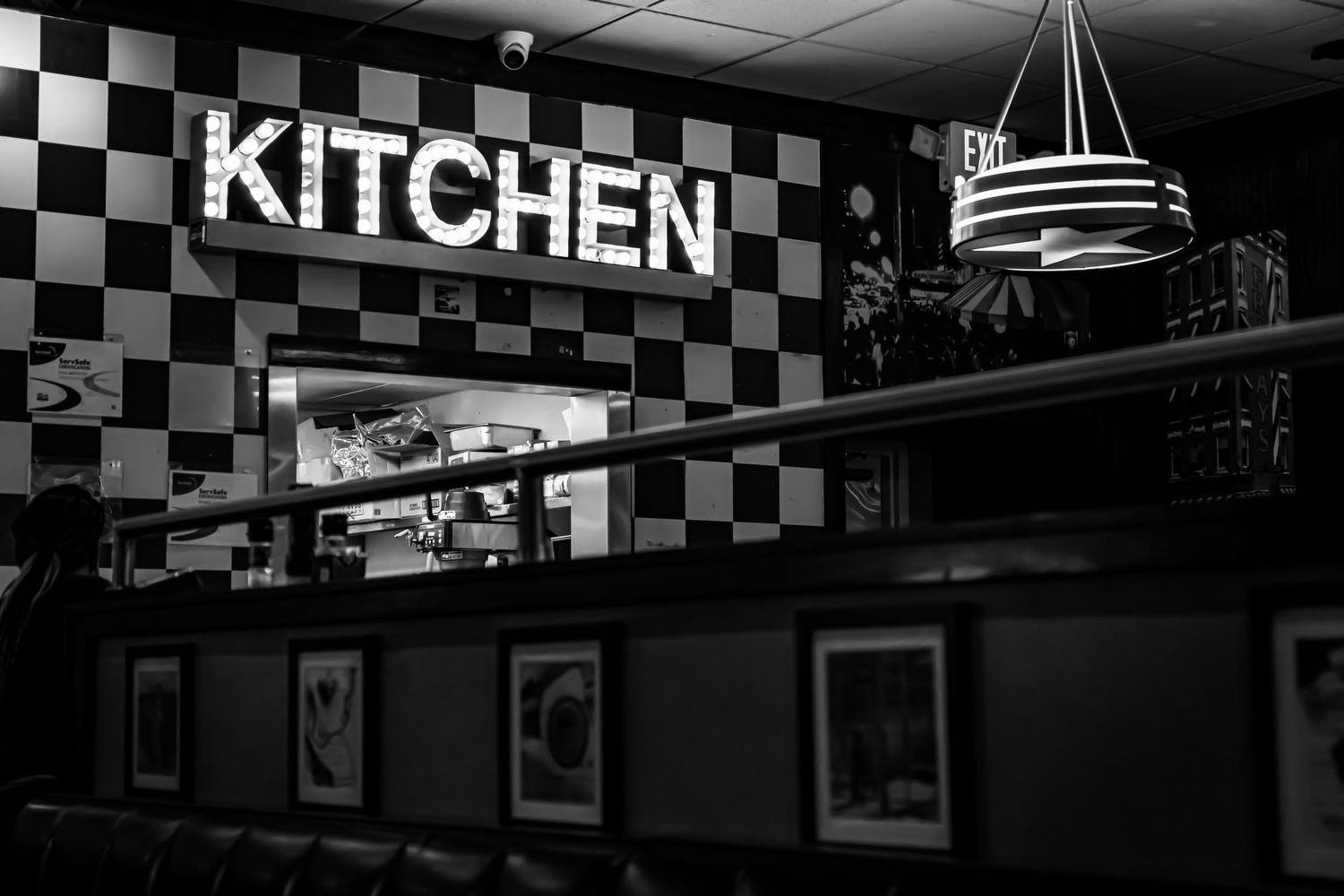 Black and white interior shot of a retro diner kitchen entrance with checkered walls and neon sign.