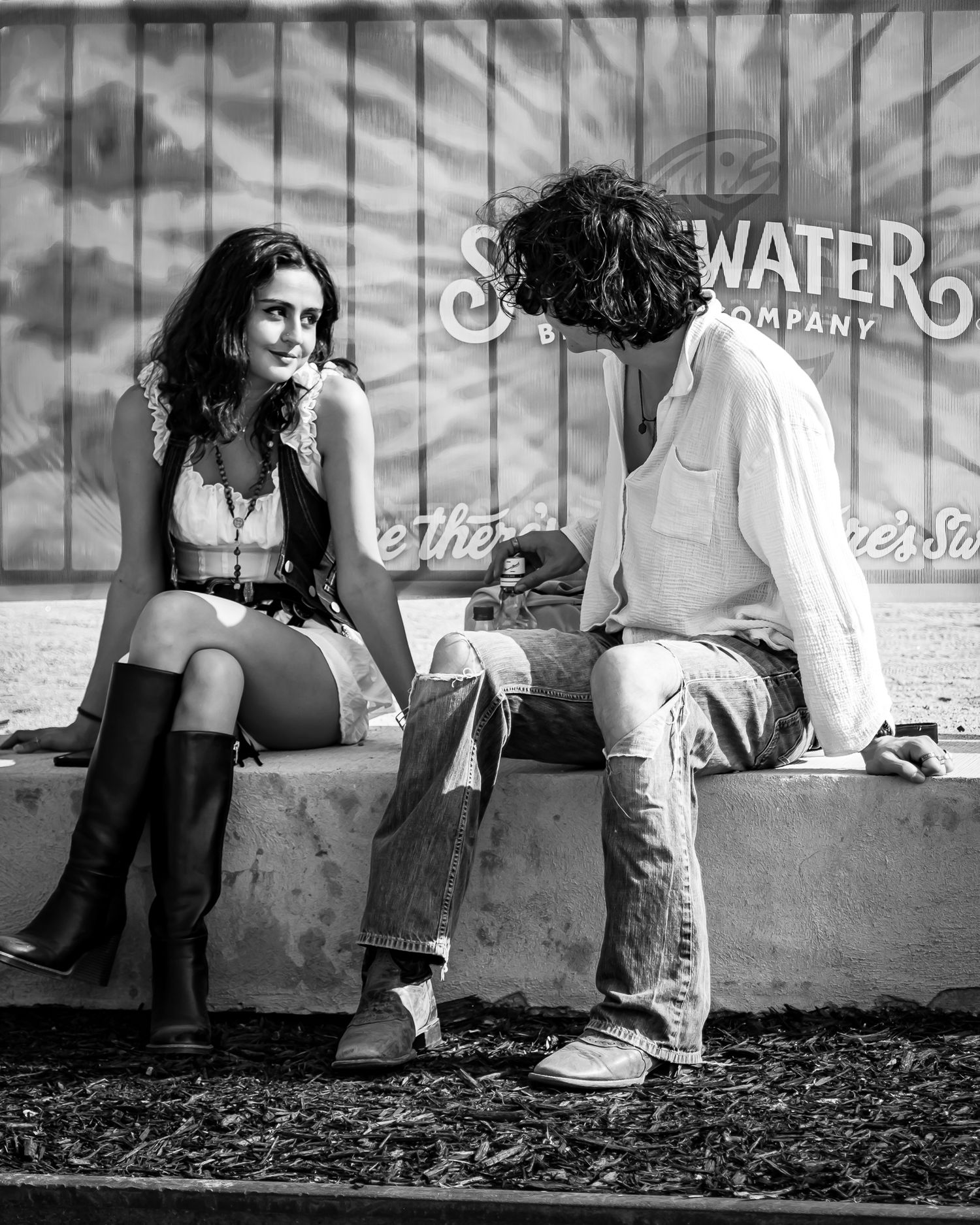 Man and woman sit together on ledge in candid black and white street photography portrait.
