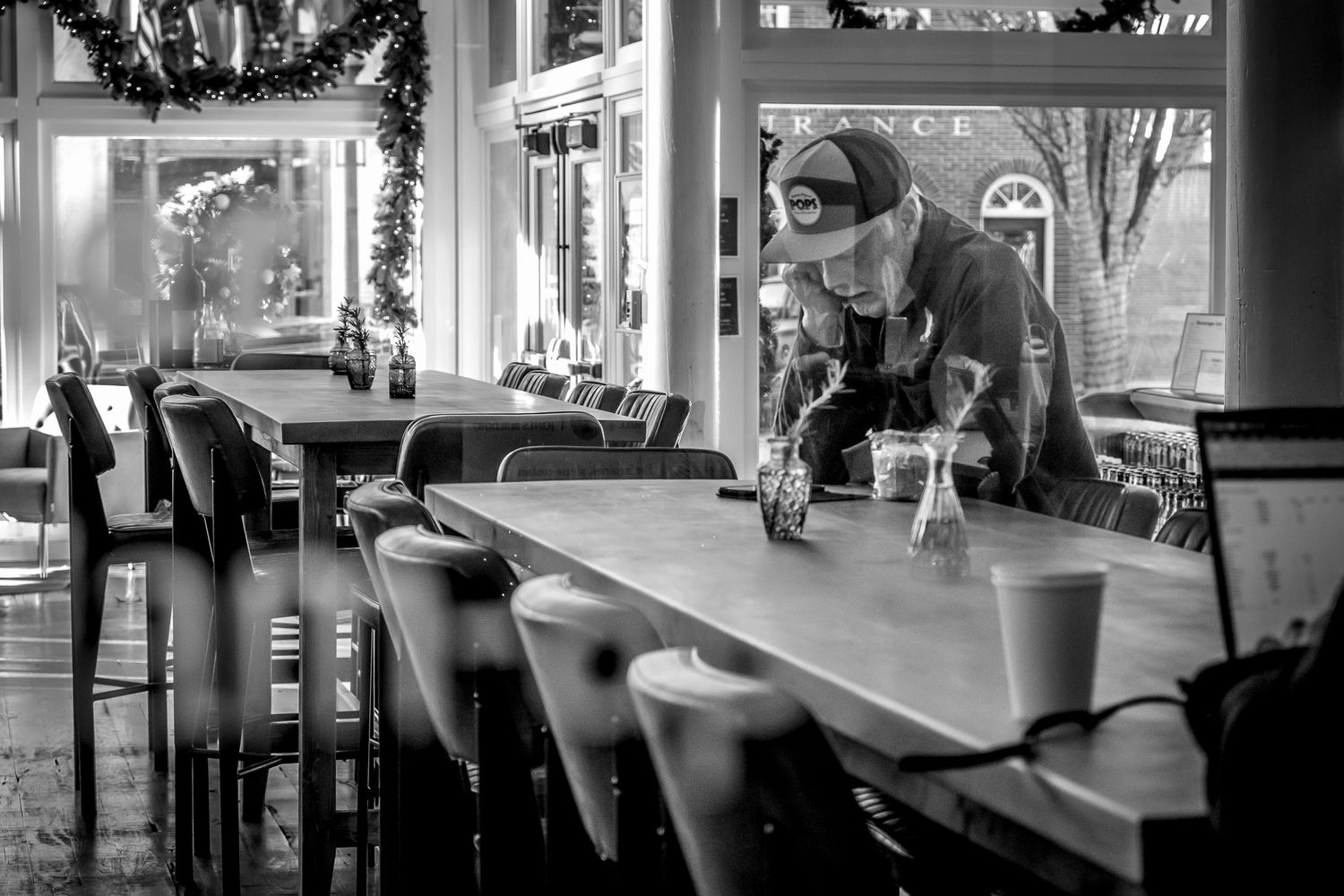 Black and white photo of a masked worker cleaning a long table in an empty restaurant interior. Street branding for restaurant client
