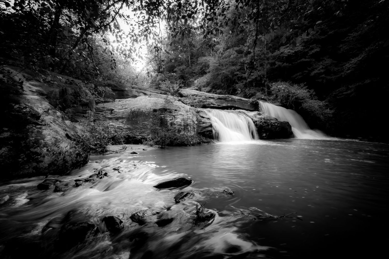 Black and white long exposure photograph of a serene waterfall cascading over rocks in a lush forest.