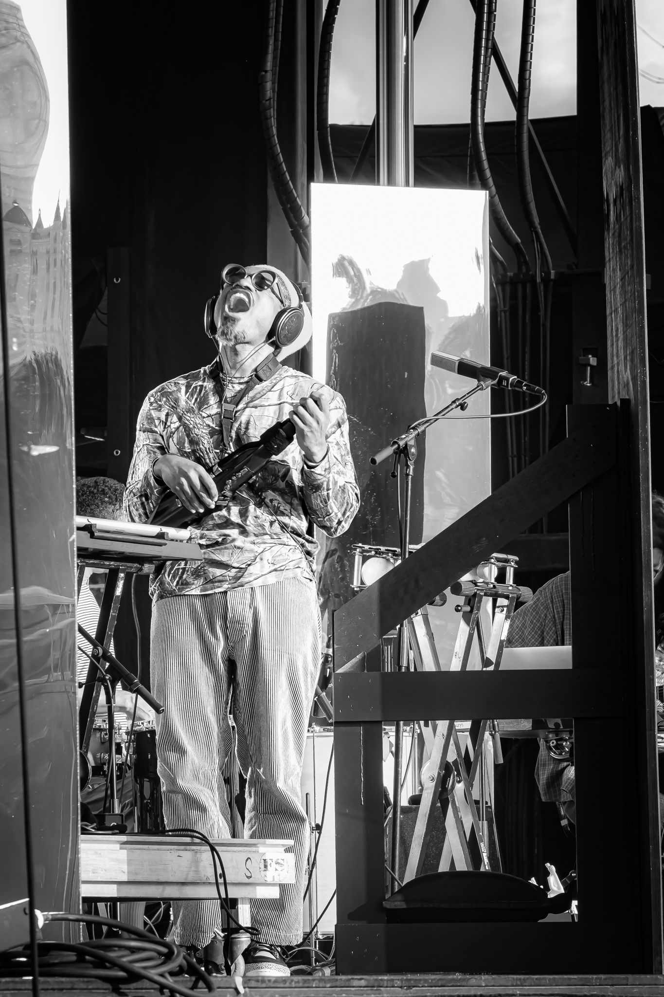 Black and white image of a performer wearing goggles and headphones playing instrument under bright stage lighting.