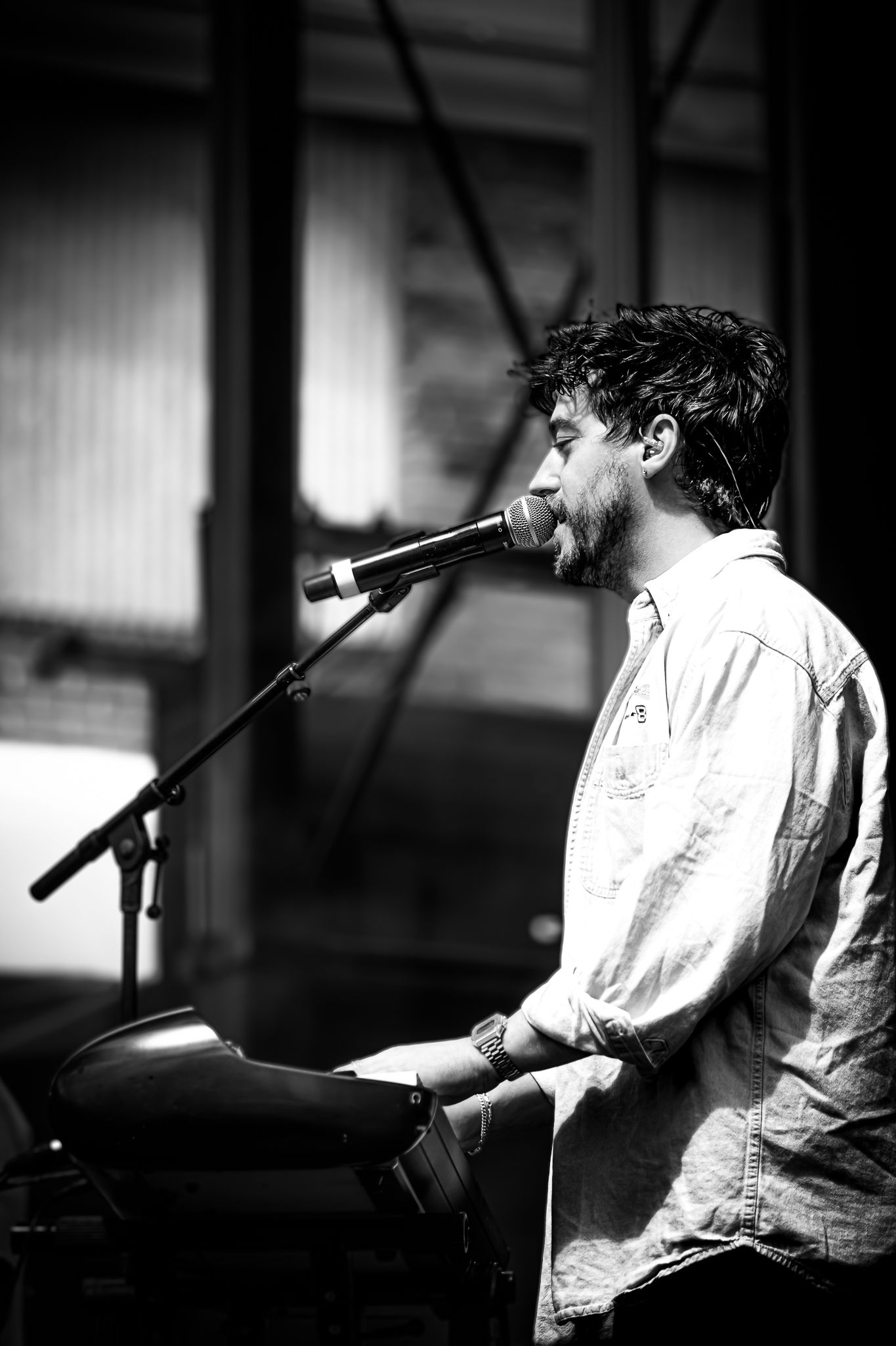 Black and white photo of a young male vocalist singing into a microphone while playing keyboard on stage.