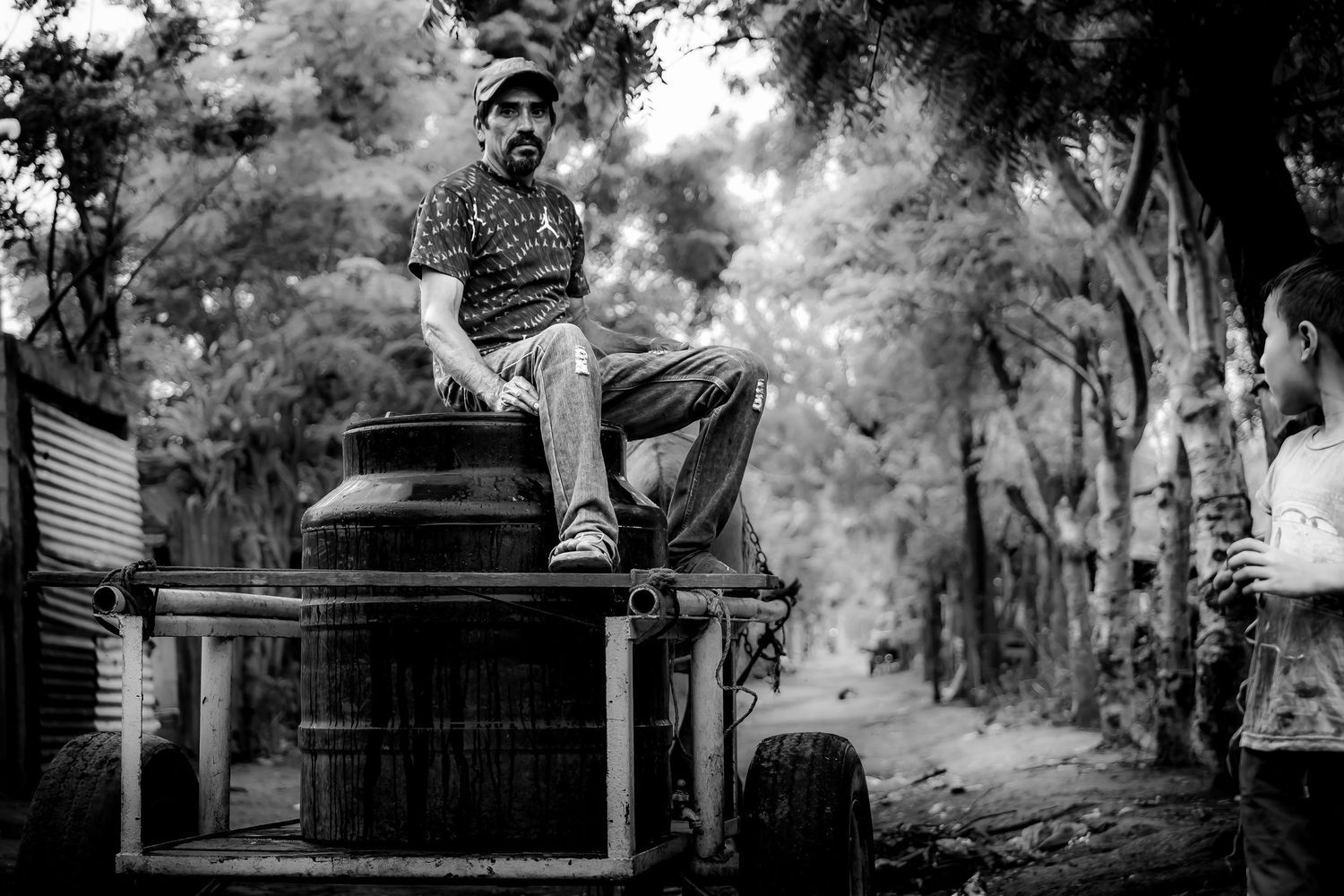 Black and white photo of a man sitting on old machinery while a child watches in a rural setting. Nicaragua. Documentary. Missions.