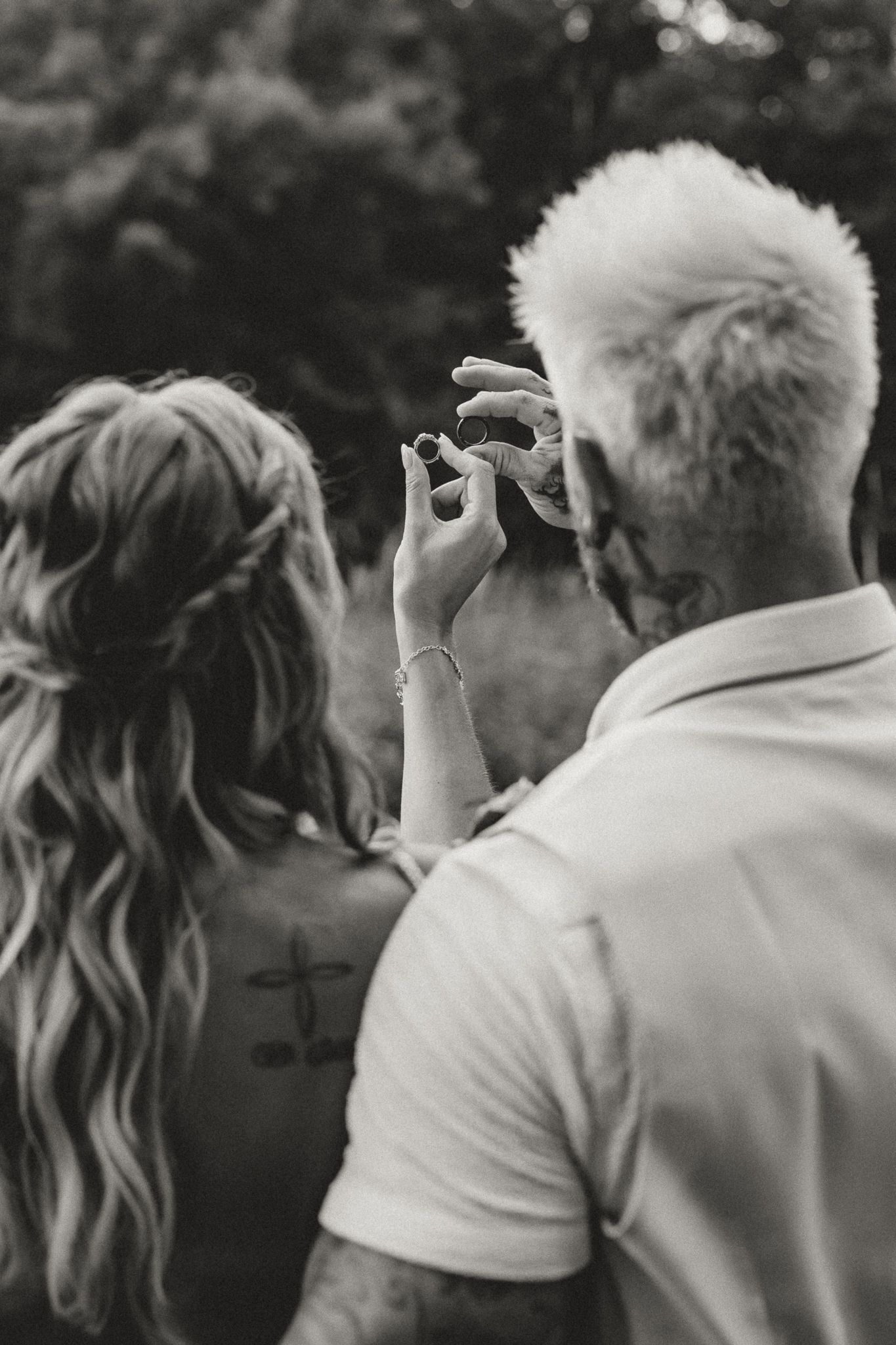 Black and white photo of a couple, woman with braided hair and cross tattoo, man with bleached hair, sharing an intimate moment outdoors.