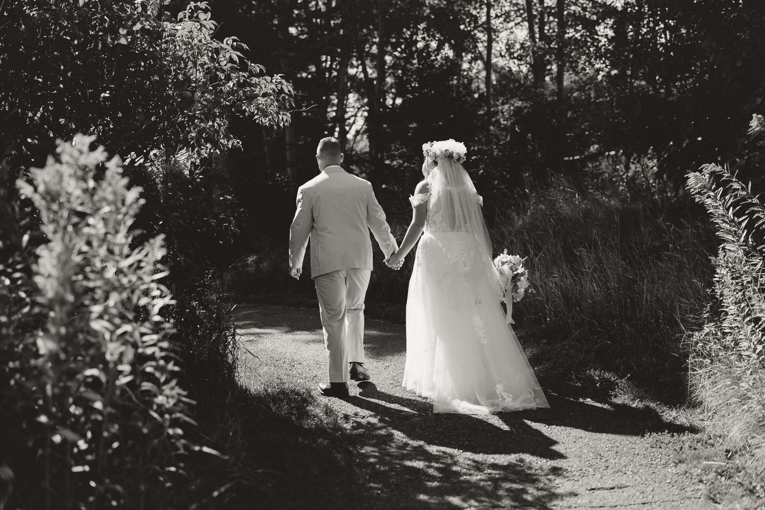 Black and white photo of bride and groom walking hand in hand down a garden path on their wedding day.
