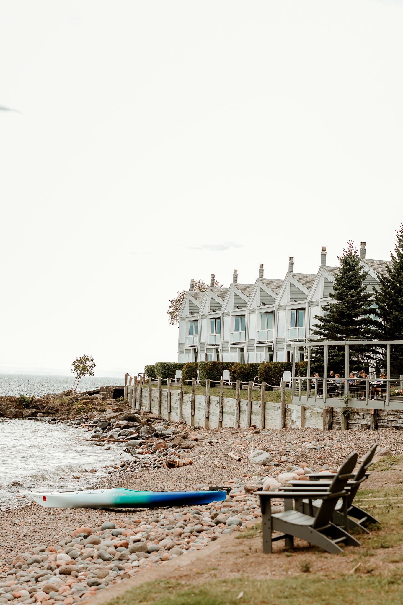 Waterfront inn with Adirondack chairs and kayak on rocky beach shore at dusk.