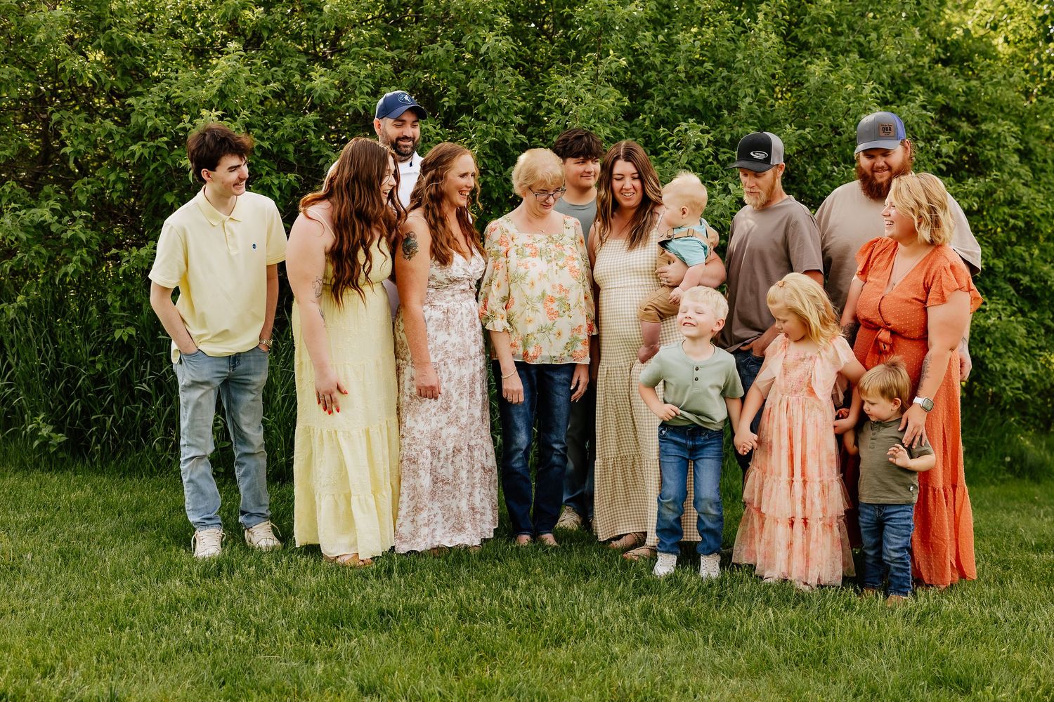Multigenerational family gathering outdoors on grass, laughing and interacting in natural evening light.