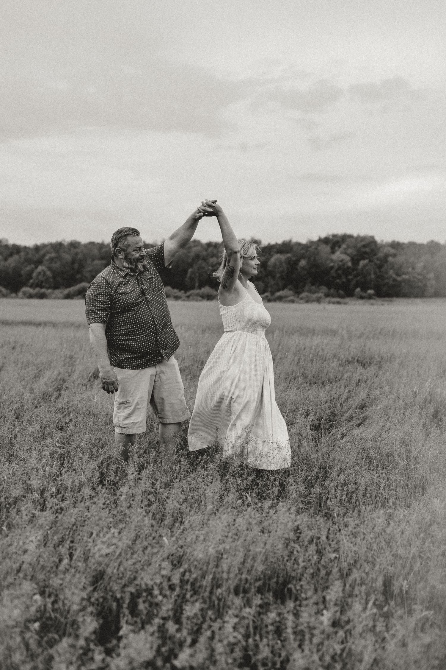 A couple dances joyfully in a vast open field, captured in a romantic black and white countryside photograph.