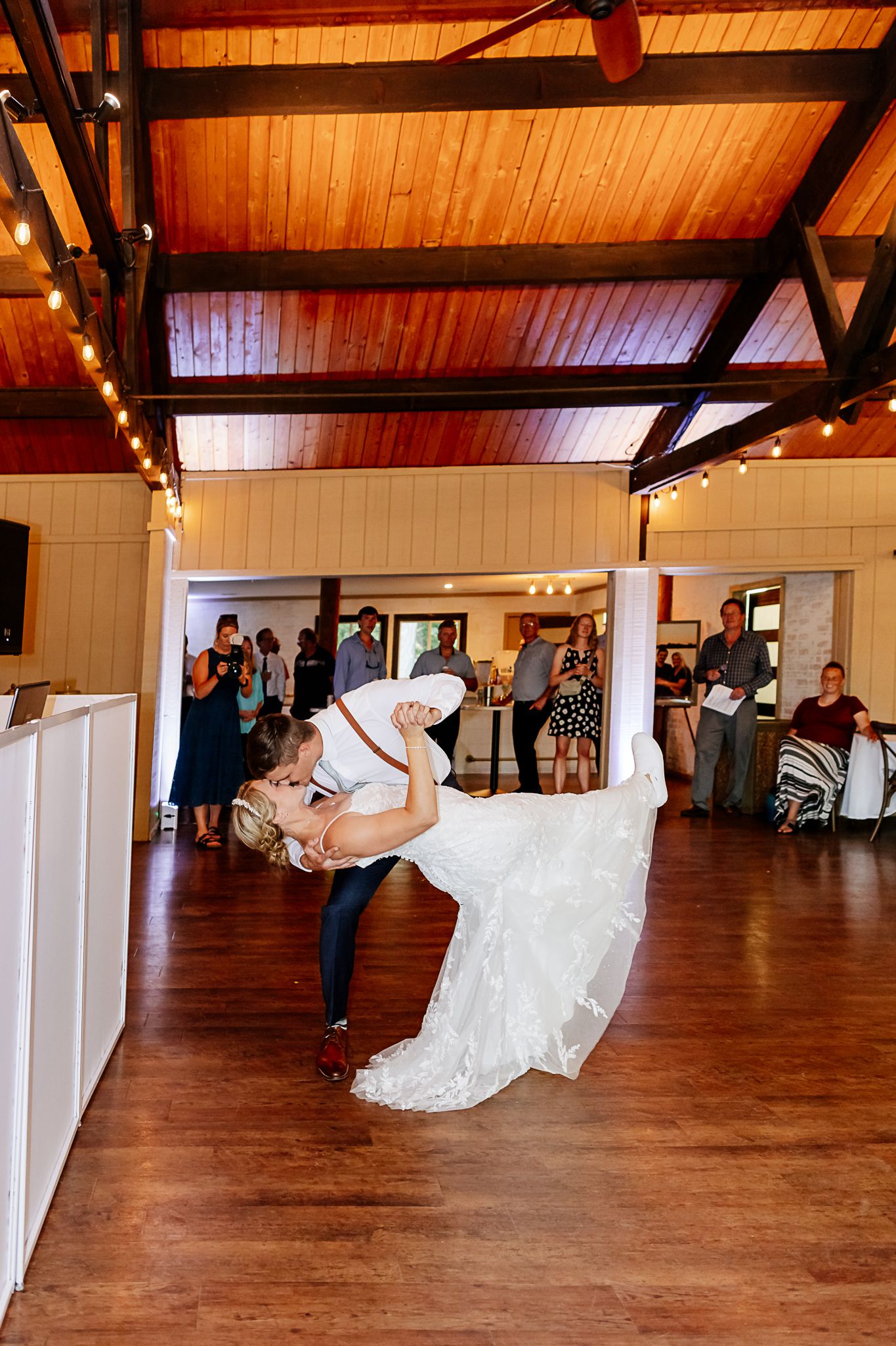 Bride and groom share a romantic dip during their first dance at a rustic wedding reception venue.