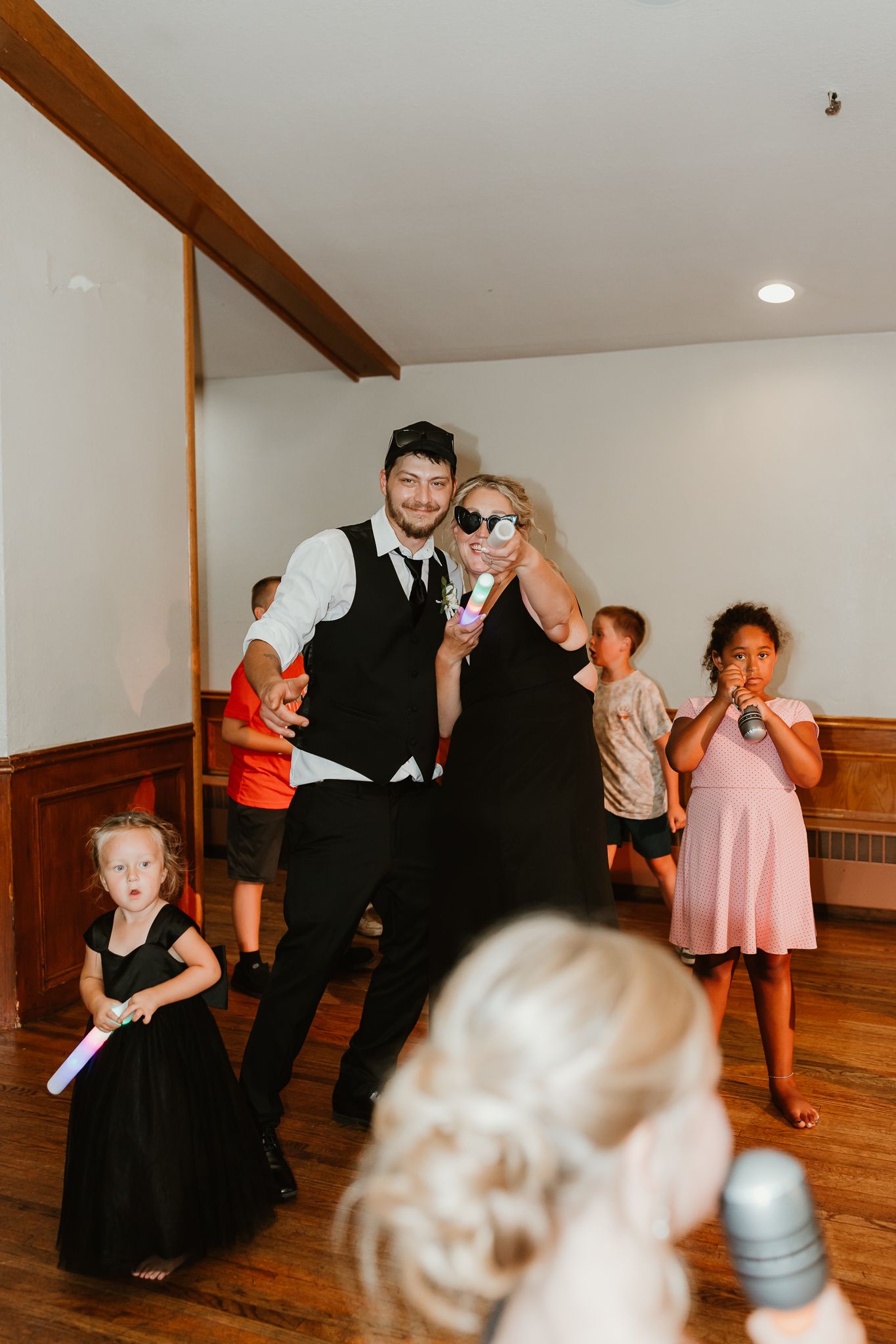 Couple in formal attire poses with children on a wooden dance floor at a wedding reception.