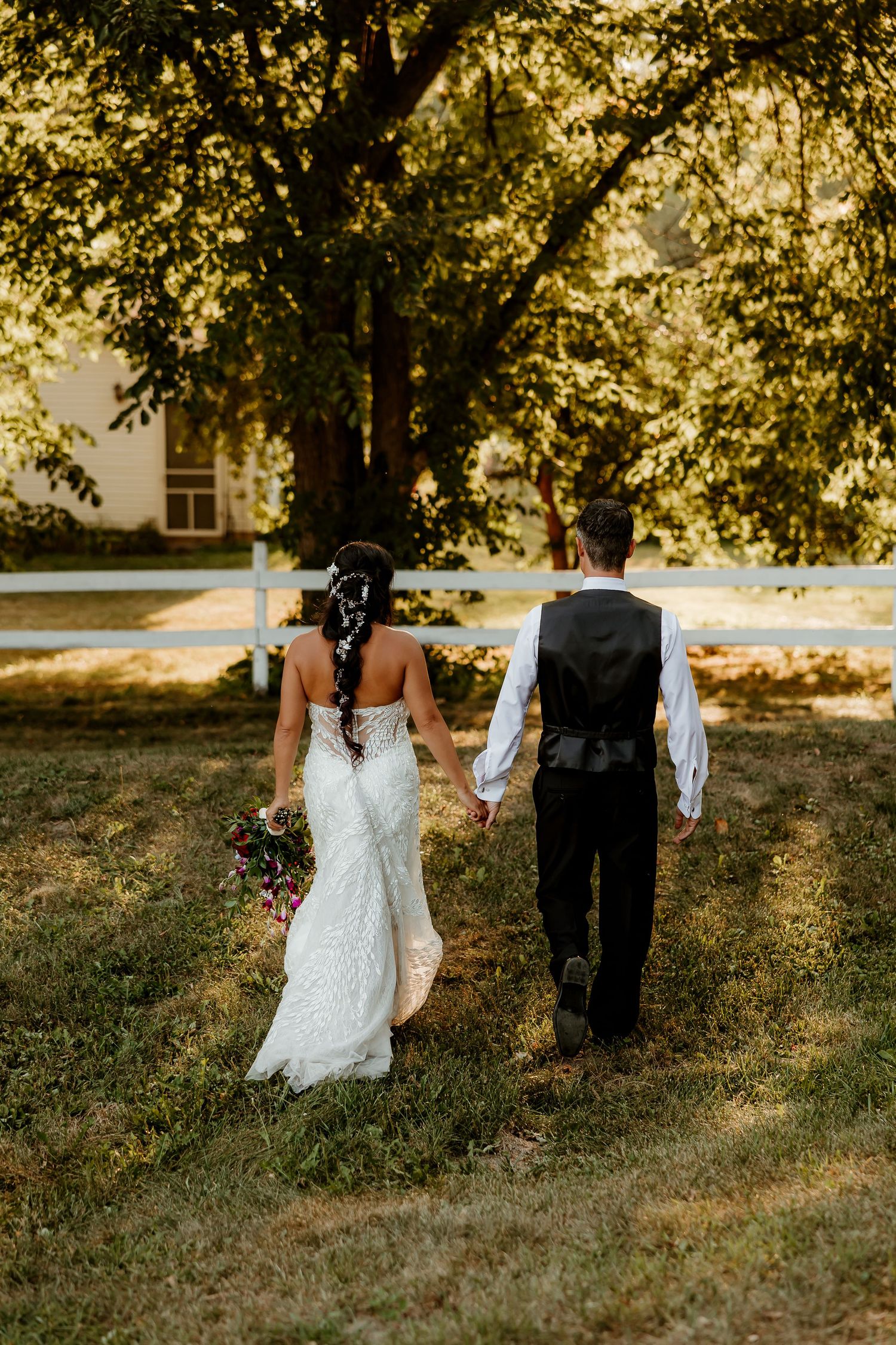 Bride and groom walking hand in hand through a sunlit garden, bride in lace gown holding bouquet.