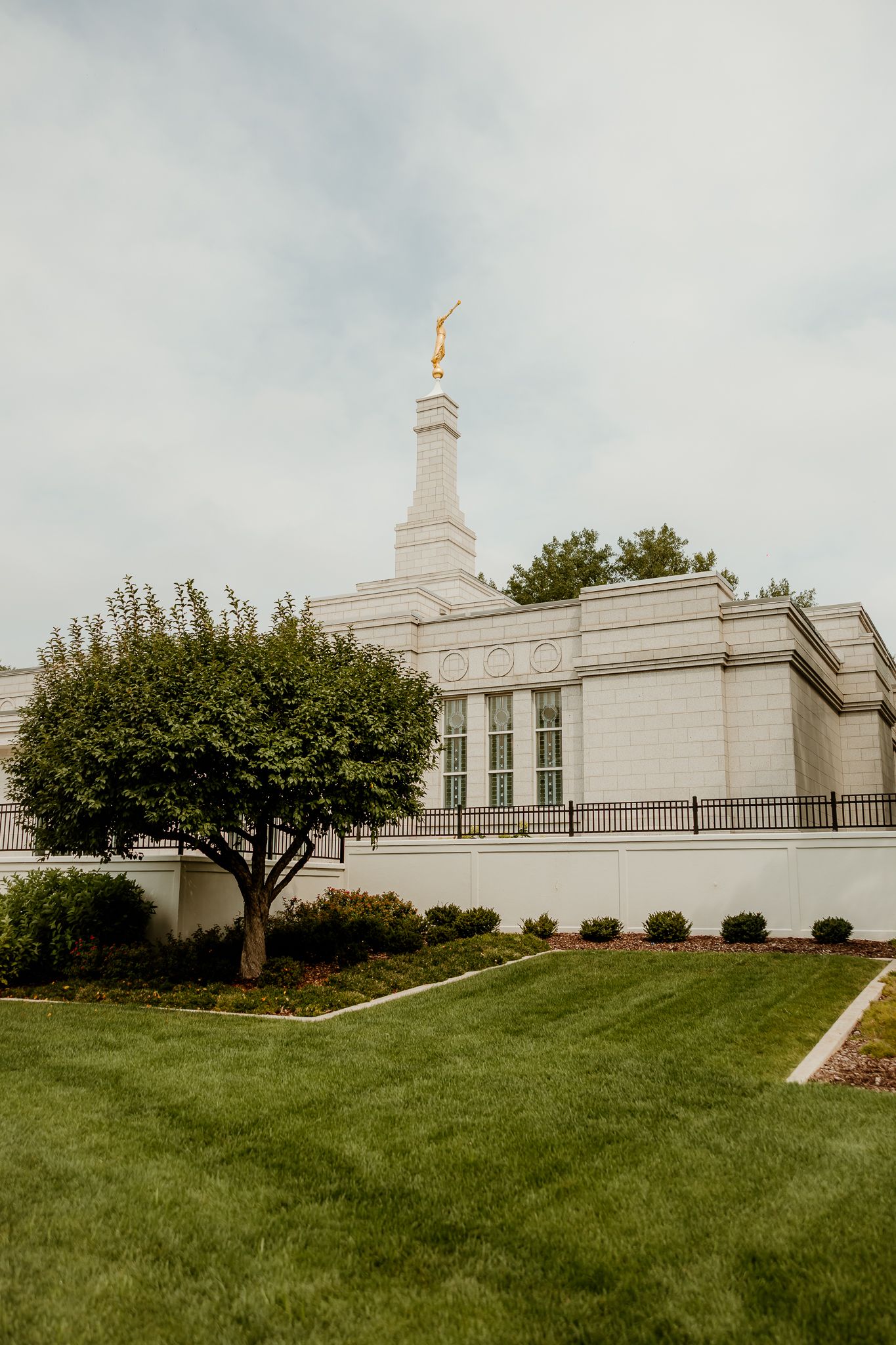 White LDS temple with gold angel Moroni statue atop spire, surrounded by manicured green lawn and trees.