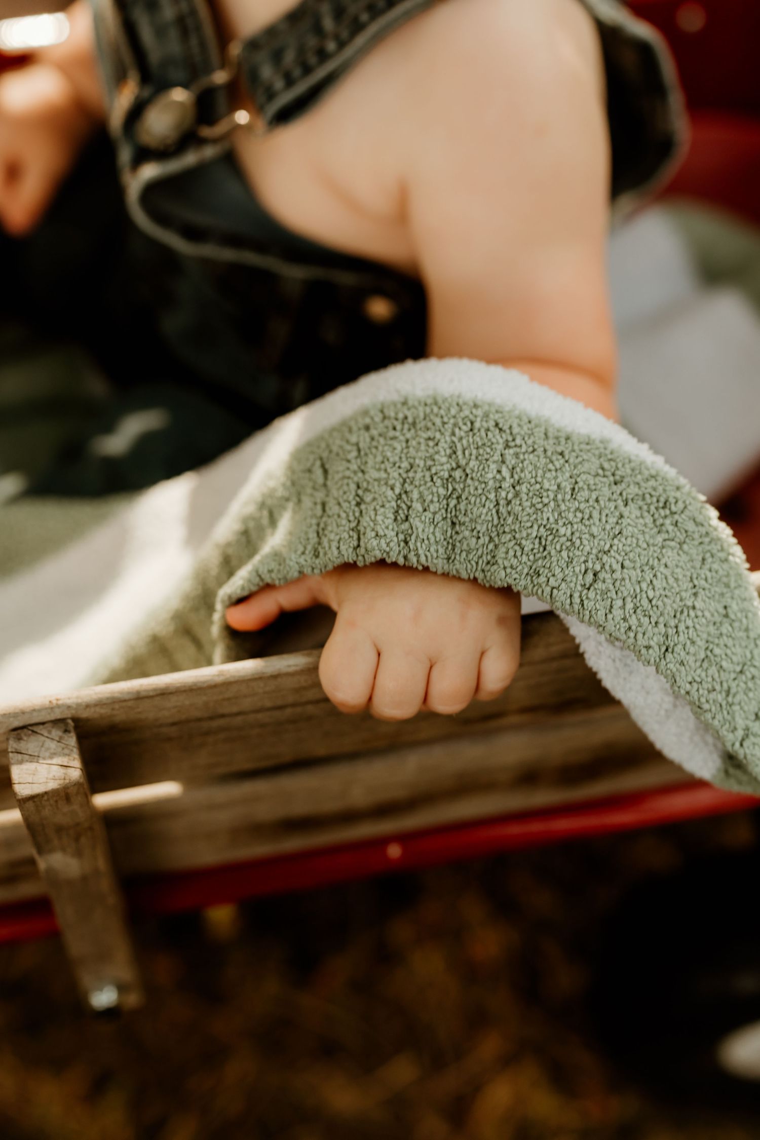Close-up of a baby's tiny hand resting on a wooden sled edge, partially covered by a soft green blanket.