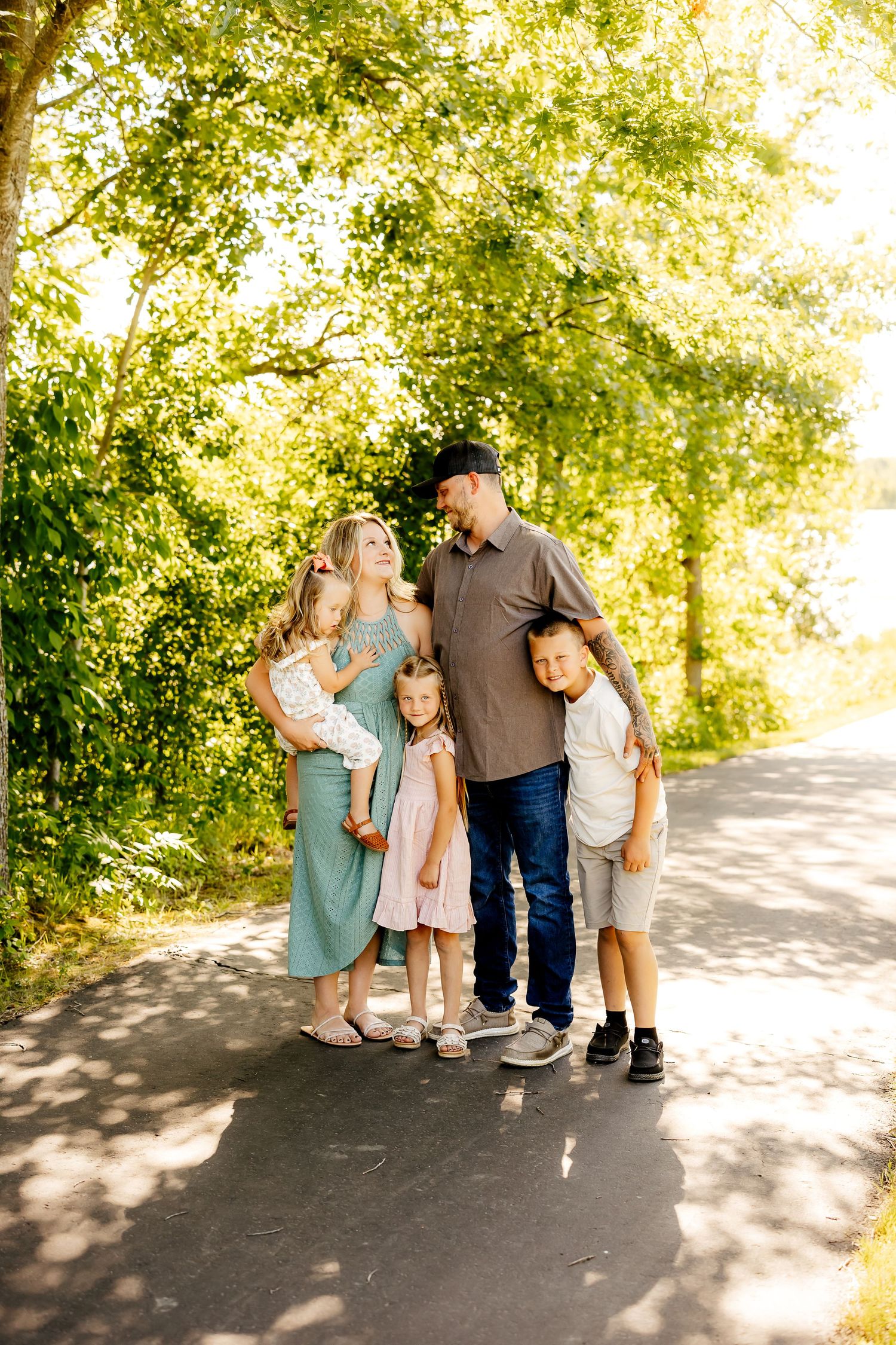 Happy family of five posing together on a sunny tree-lined path in summer.