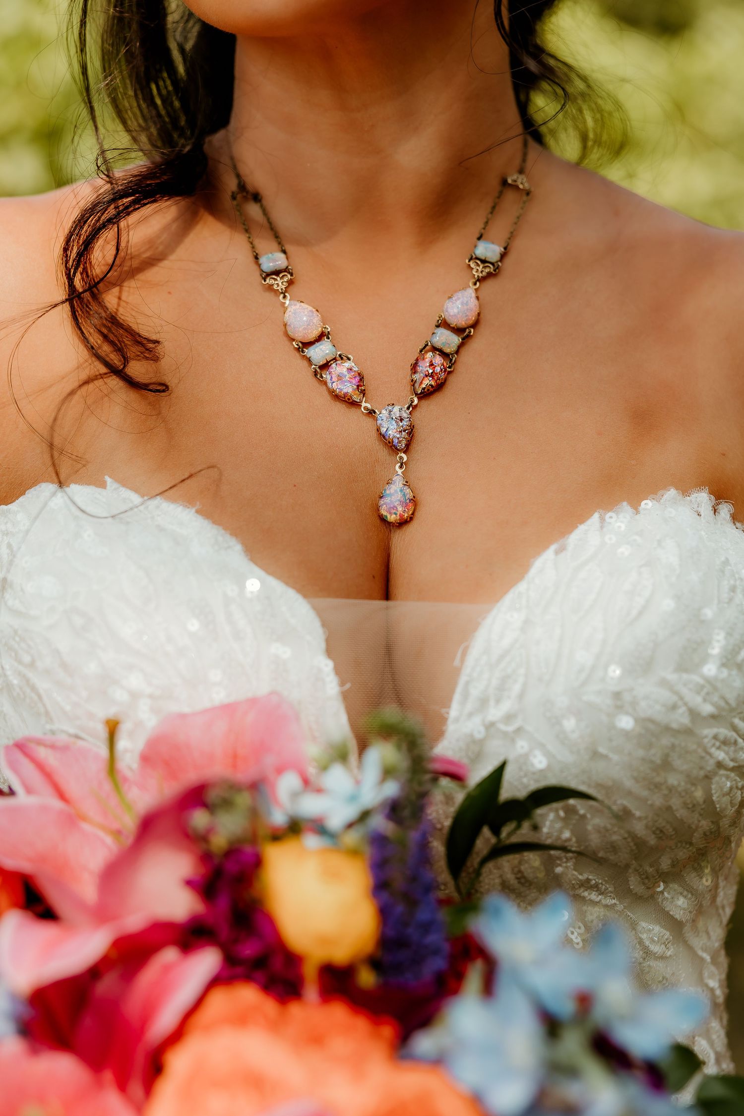 Bride in strapless lace gown wearing a delicate pink gemstone necklace, holding a colorful bridal bouquet.