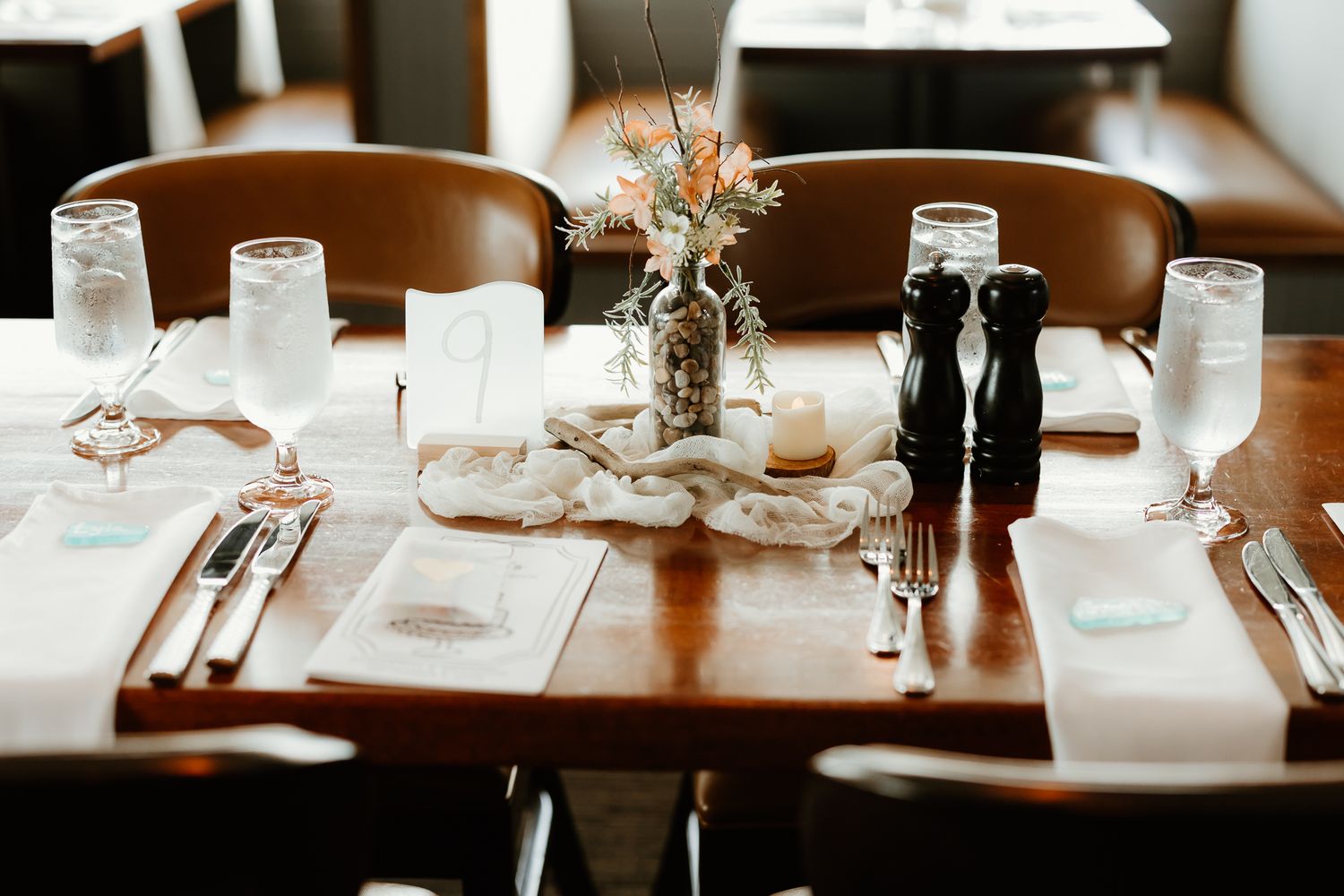 Elegant restaurant table setting with white placemats, glassware, cutlery, and a floral centerpiece on a wooden table.