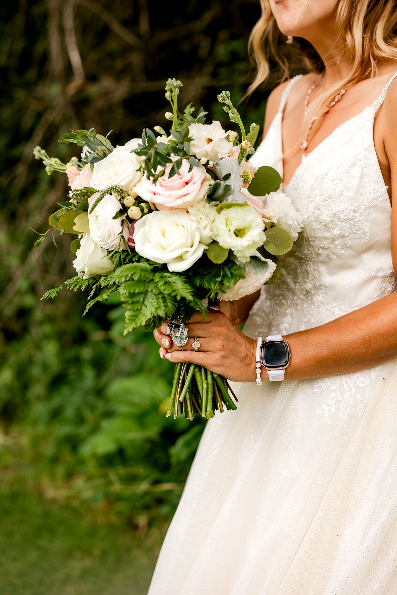 Bride in white lace gown holding elegant bouquet of white and pink roses with greenery on wedding day.