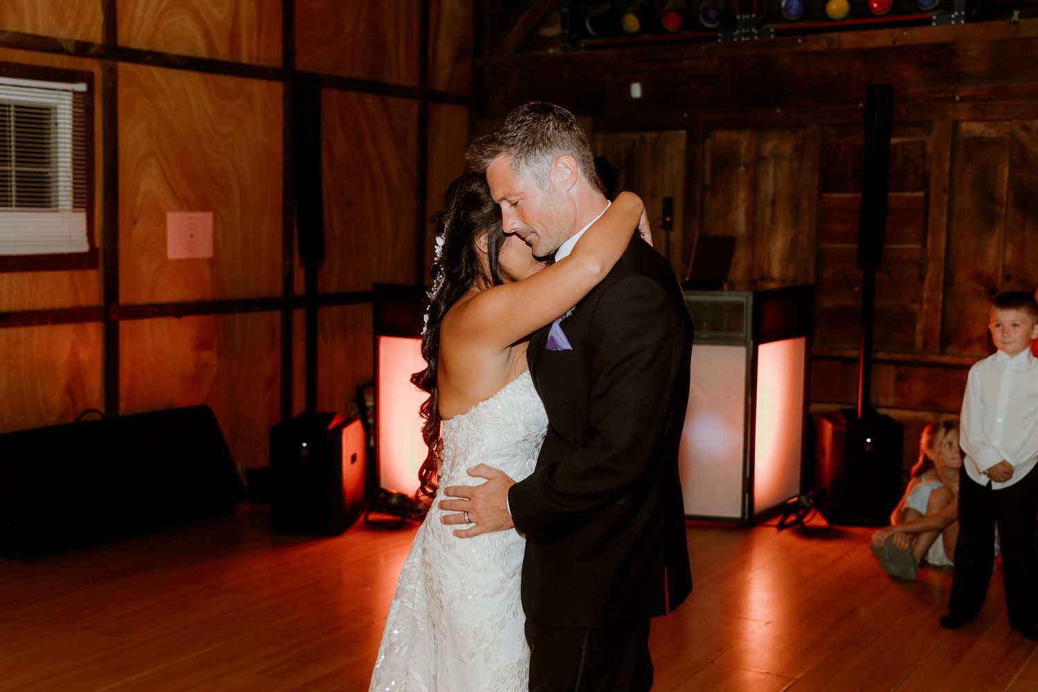 Bride and groom share their first dance in a warmly lit rustic wedding venue with wood-paneled walls.
