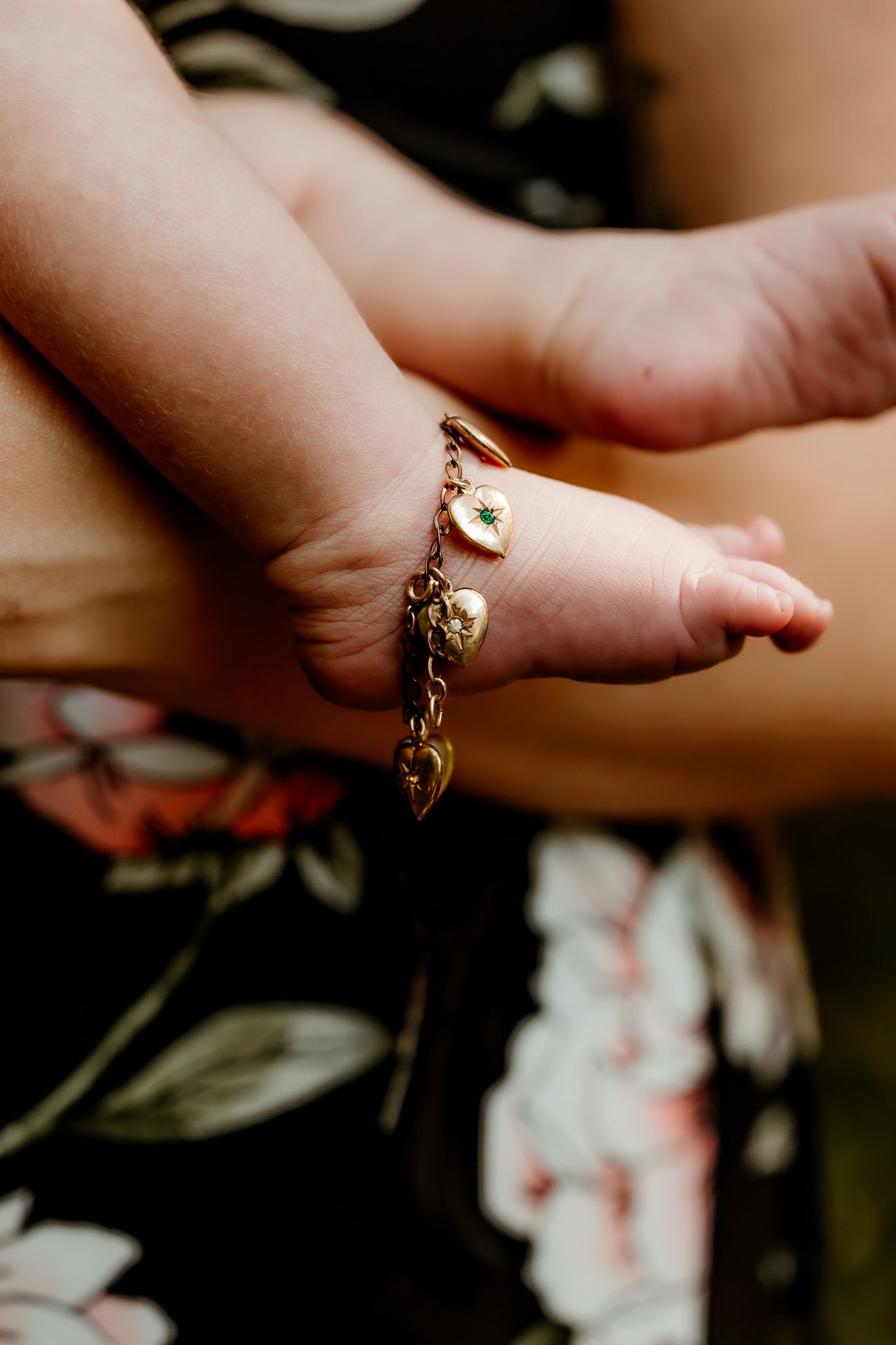 Close-up of a baby's wrist adorned with a delicate gold charm bracelet featuring heart charms.