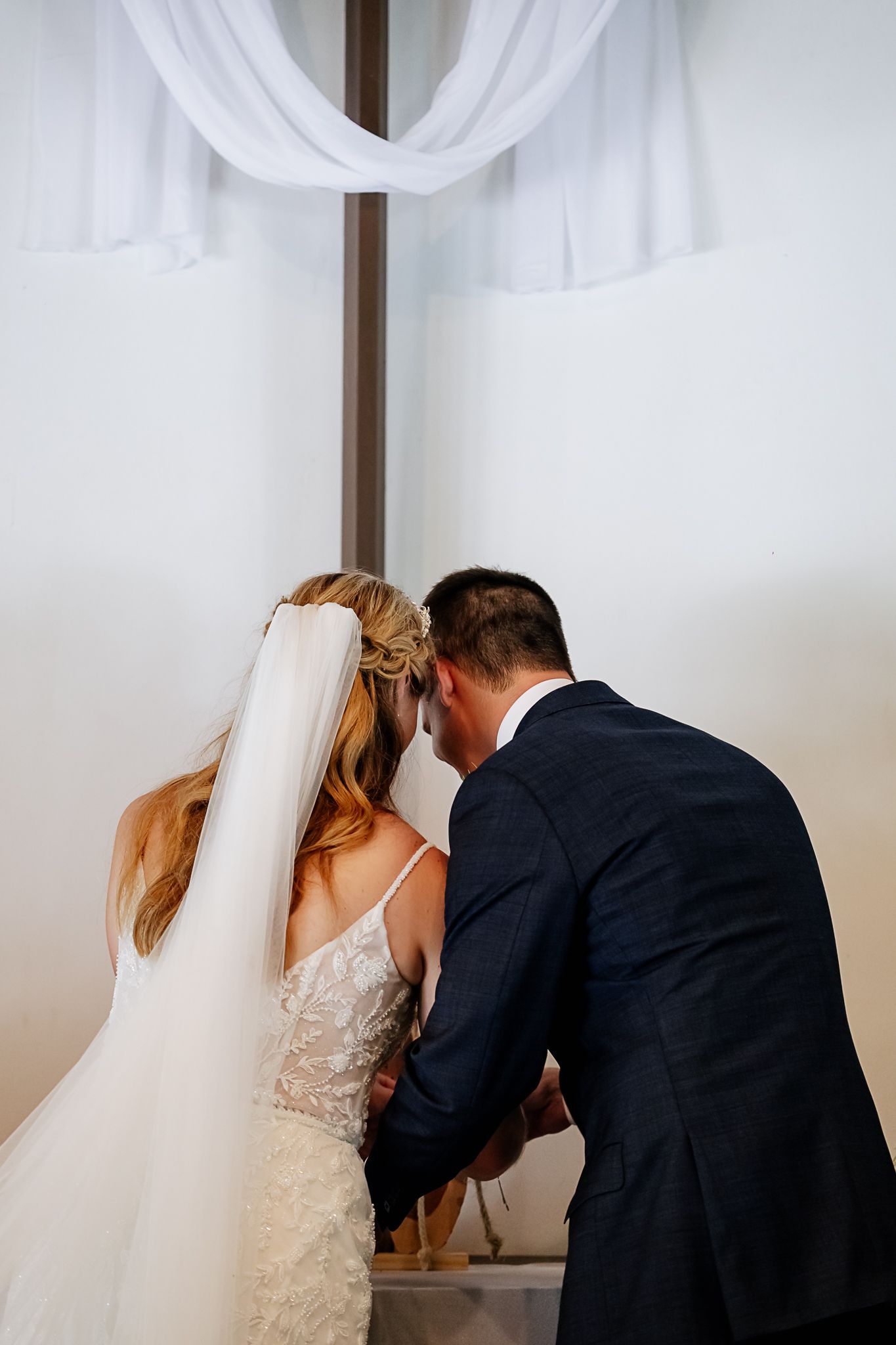 Bride and groom holding hands at the altar beneath a draped cross during their wedding ceremony.