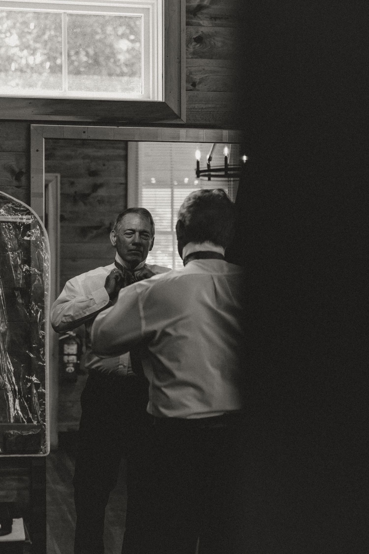 Man adjusting his tie while looking in a mirror, captured in black and white photography.