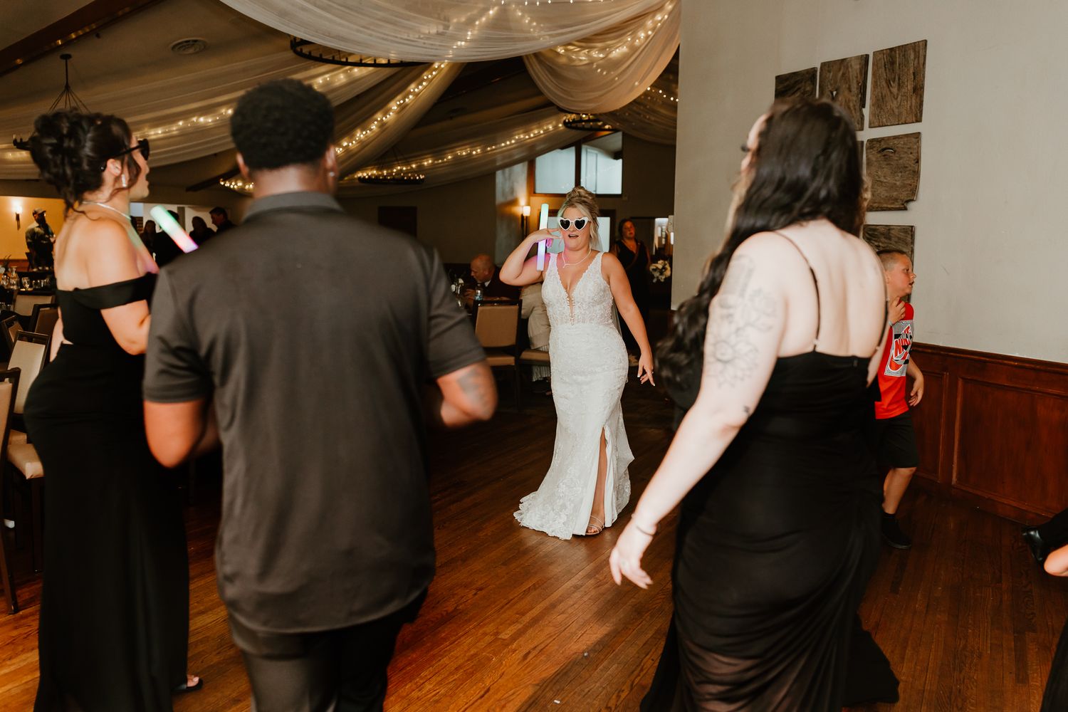Bride in white gown dancing with guests on wooden dance floor at elegant wedding reception venue.
